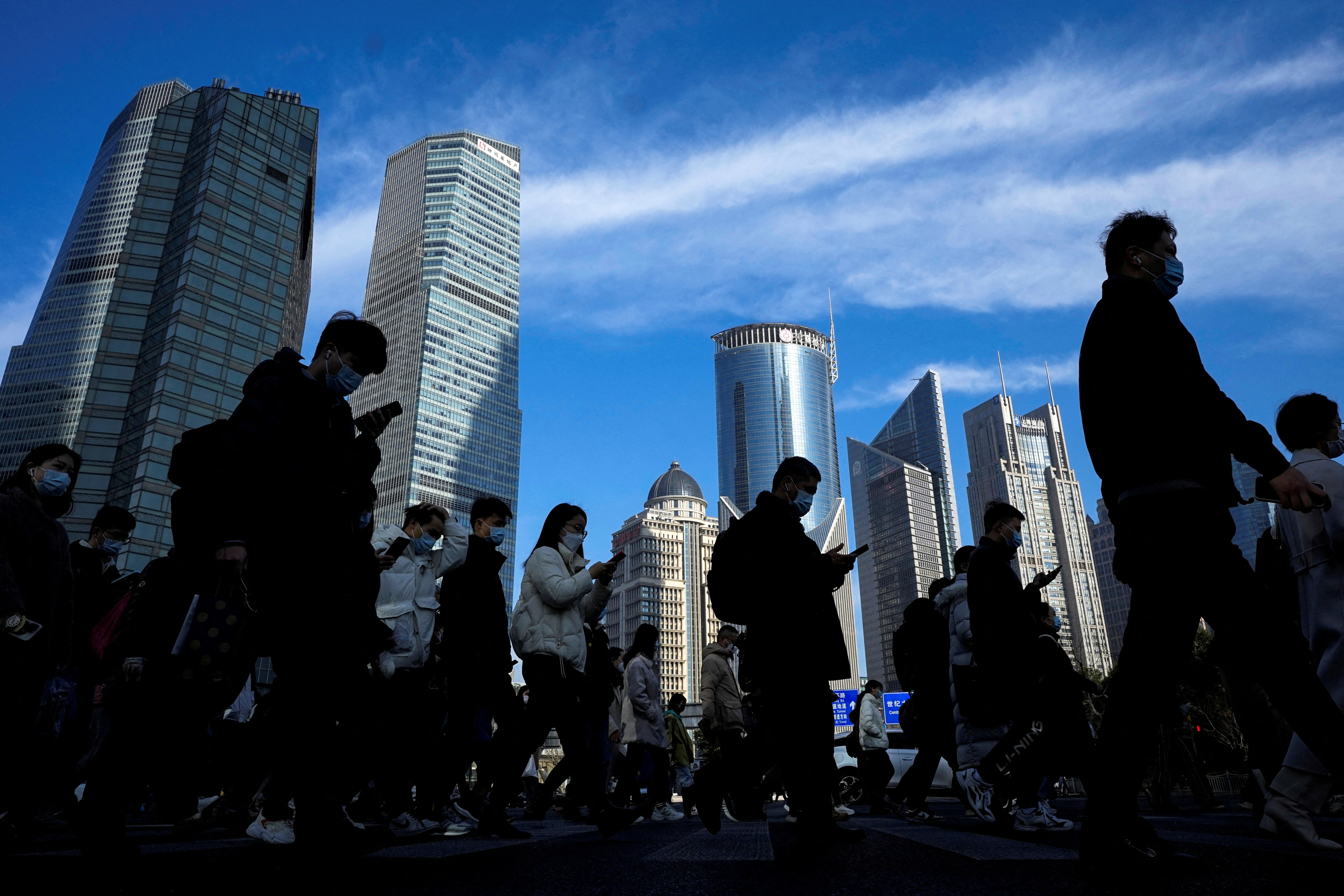 People cross a street near office towers in the Lujiazui financial district in Shanghai