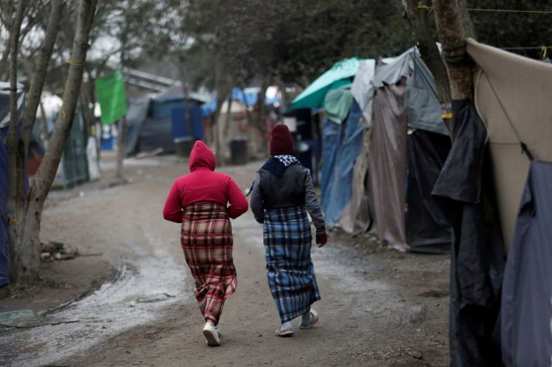 Migrant women using blankets as skirts walk inside a migrant encampment in Matamoros