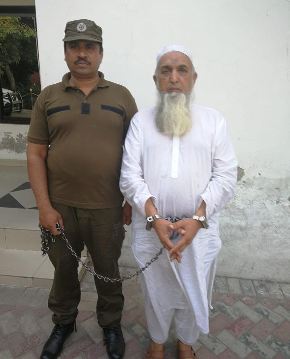 A police officer escorts handcuffed Aziz-ur-Rehman in Lahore,