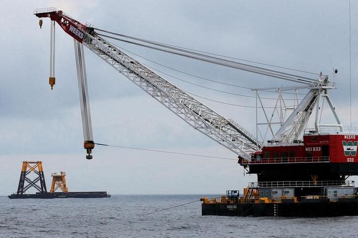 Construction crane floats next to a barge carrying jacket support structures and a platform for a turbine for a wind farm in the waters of the Atlantic Ocean off Block Island, Rhode Island