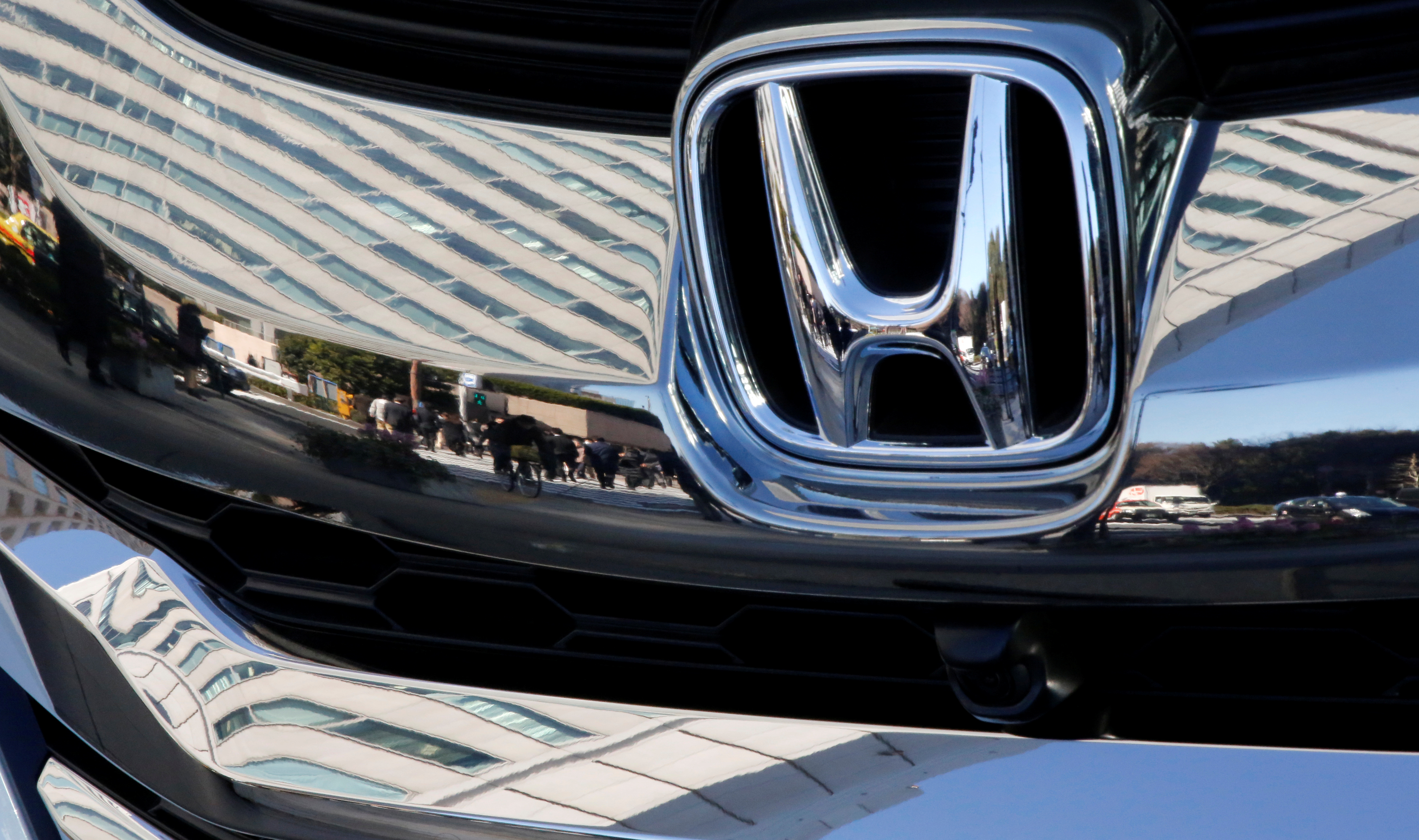 People are reflected on a Honda Motor car outside the company's headquarters in Tokyo