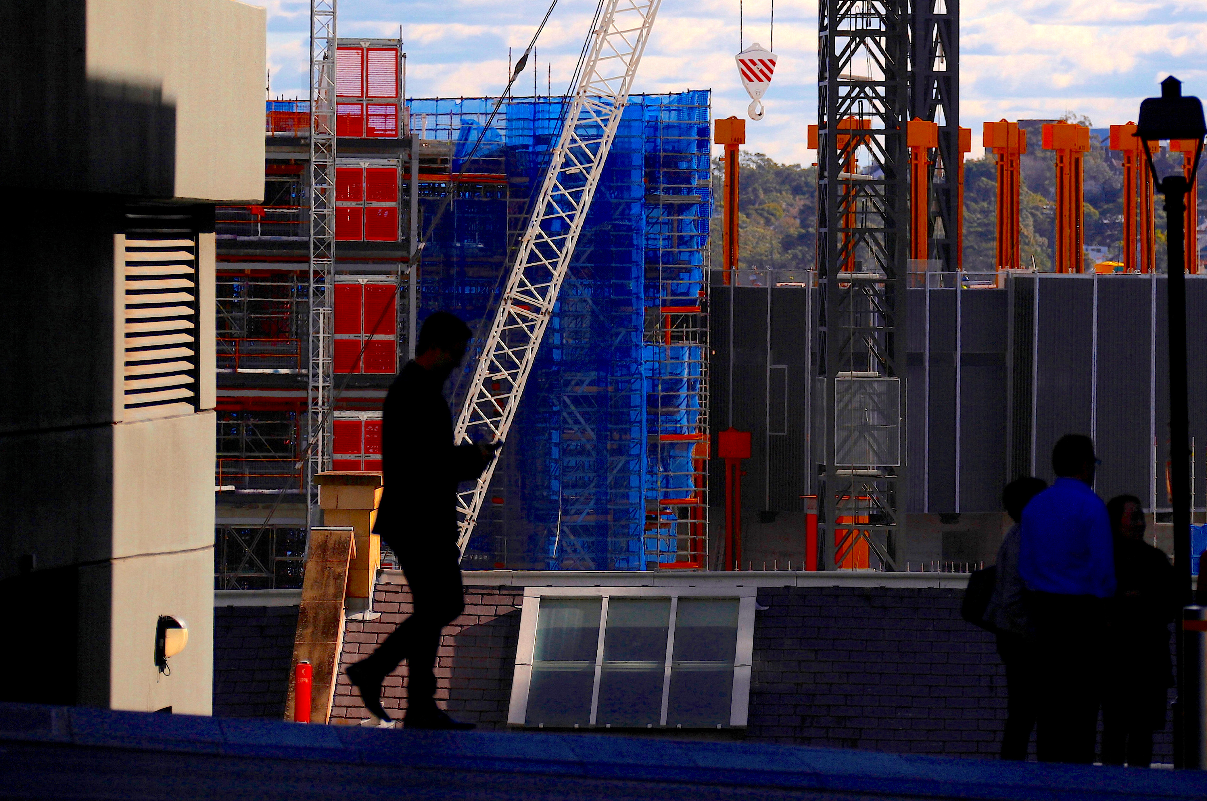 Pedestrians walk in front of a crane and scaffolding on a construction site in central Sydney