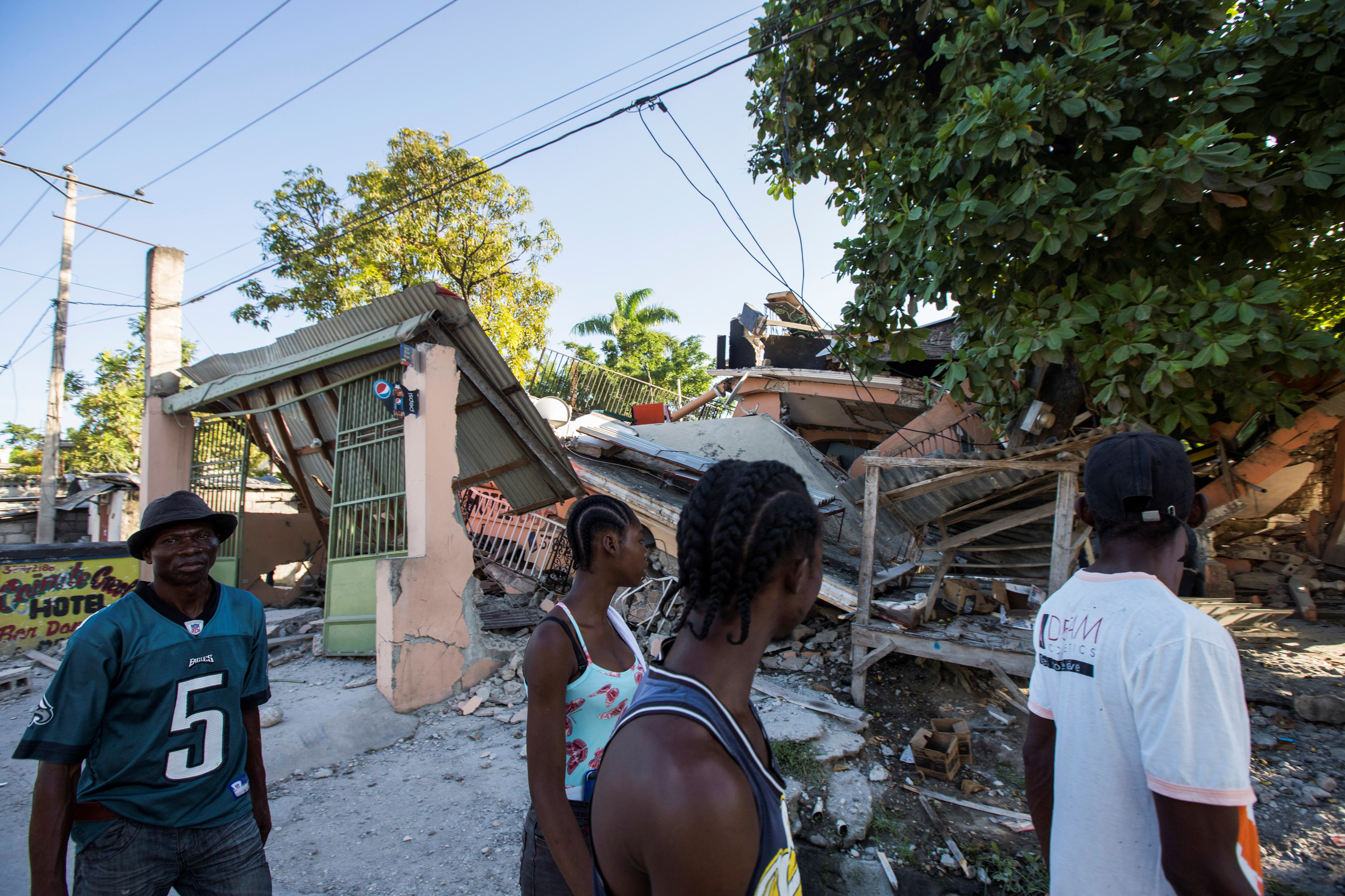 People walk past a house destroyed following a 7.2 magnitude earthquake in Les Cayes, Haiti August 14, 2021. REUTERS/Ralph Tedy Erol  