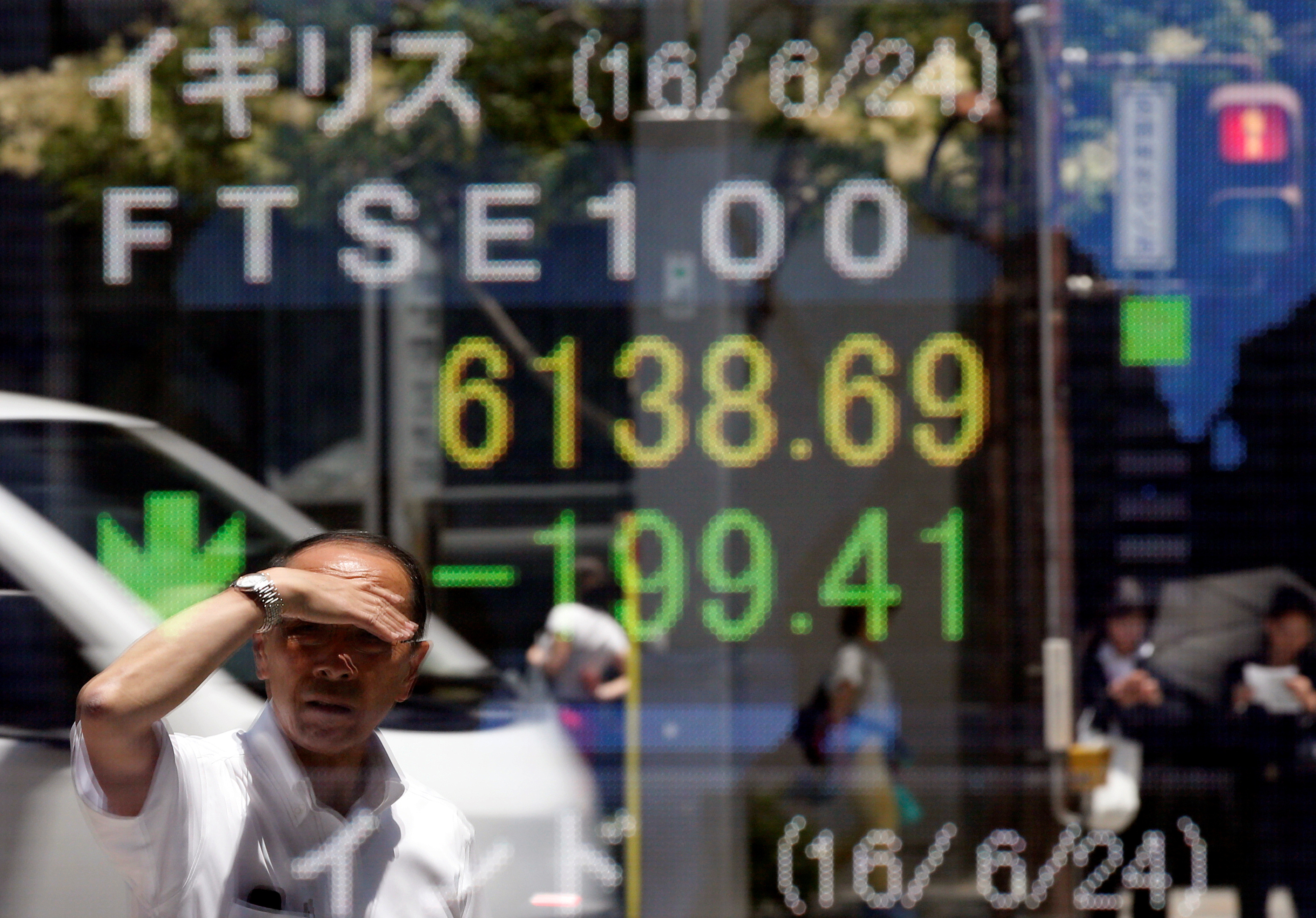 A man is reflected in an electronic board showing Britain's FTSE 100 outside a brokerage in Tokyo