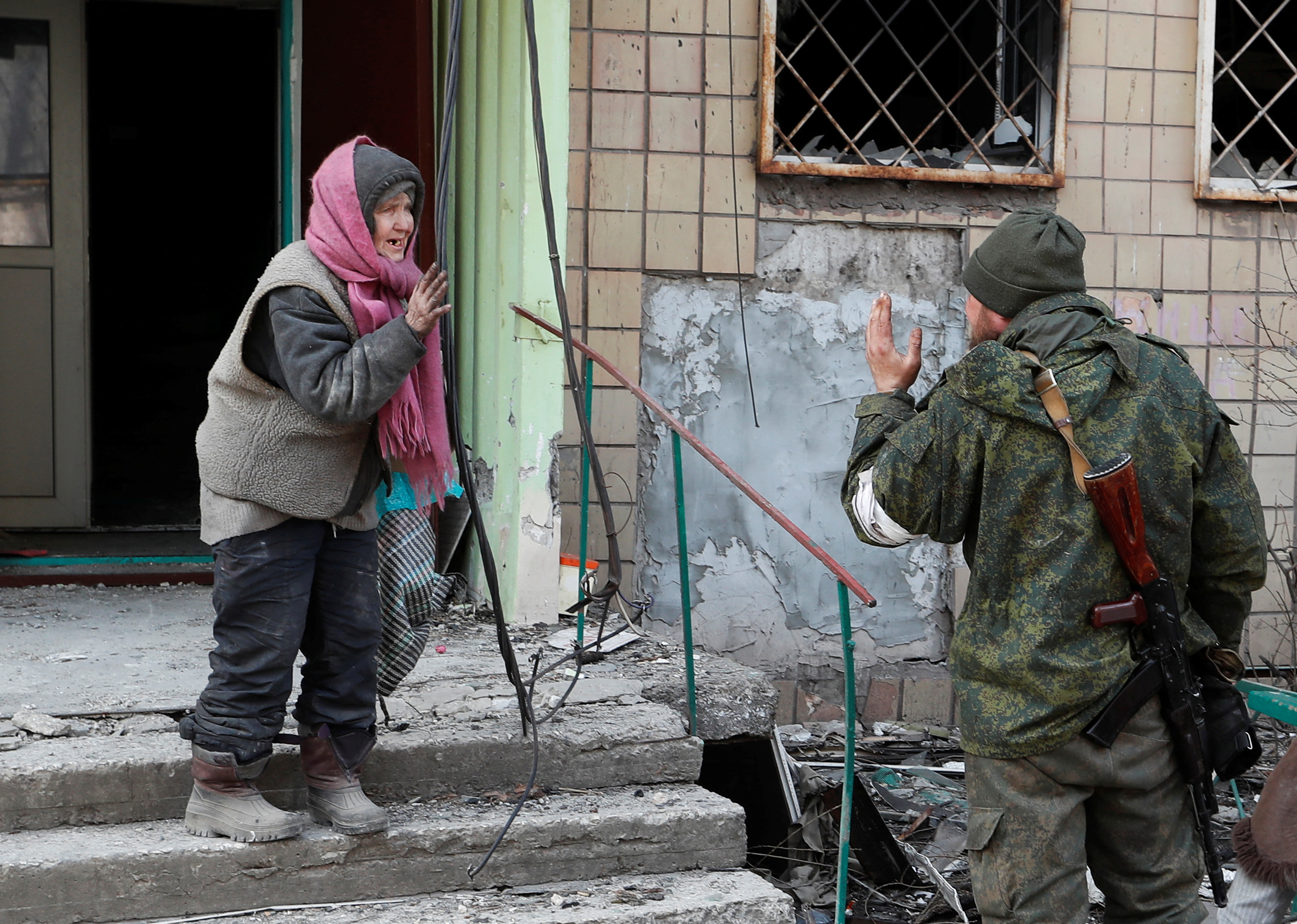 A local resident speaks to a service member of pro-Russian troops outside a damaged apartment building in Mariupol
