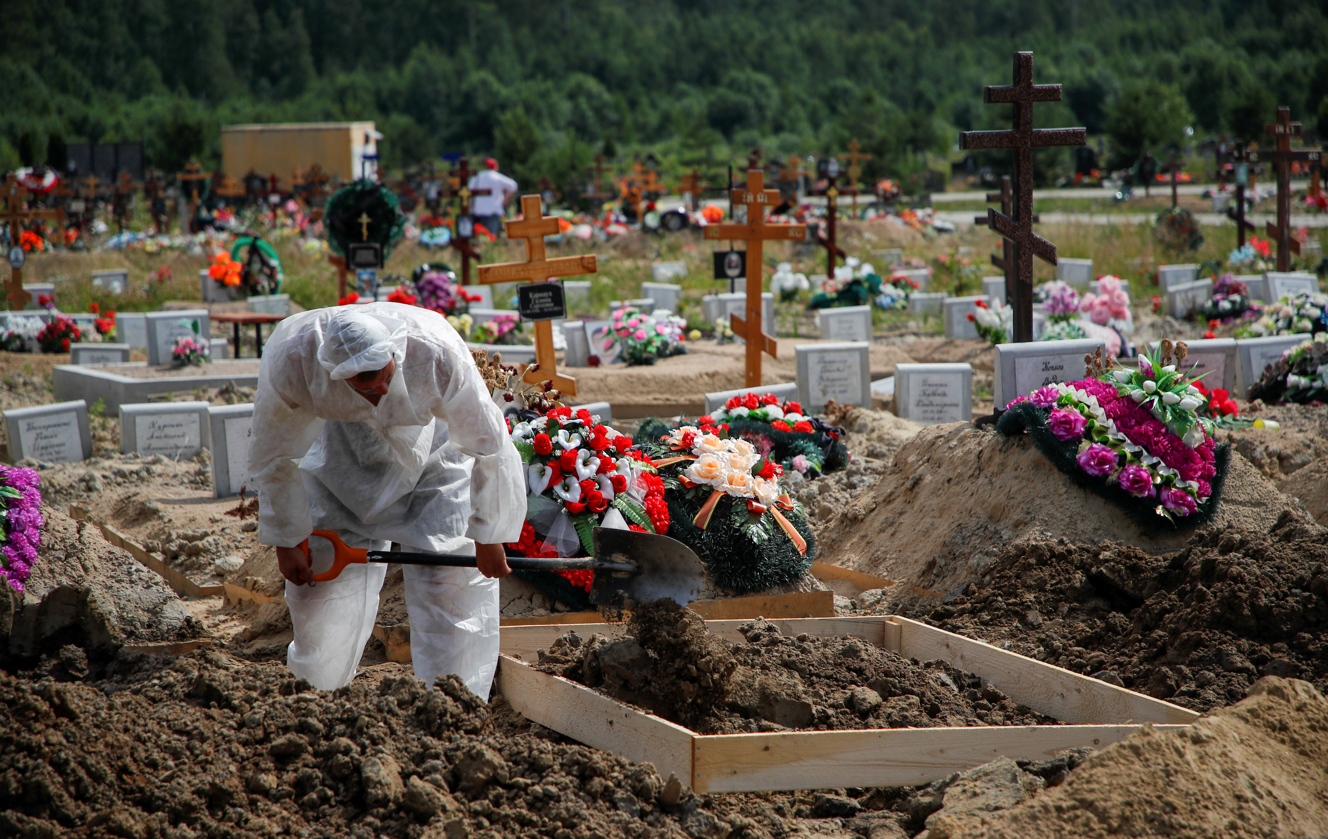 A grave digger wearing personal protective equipment buries a person at a graveyard in Saint Petersburg