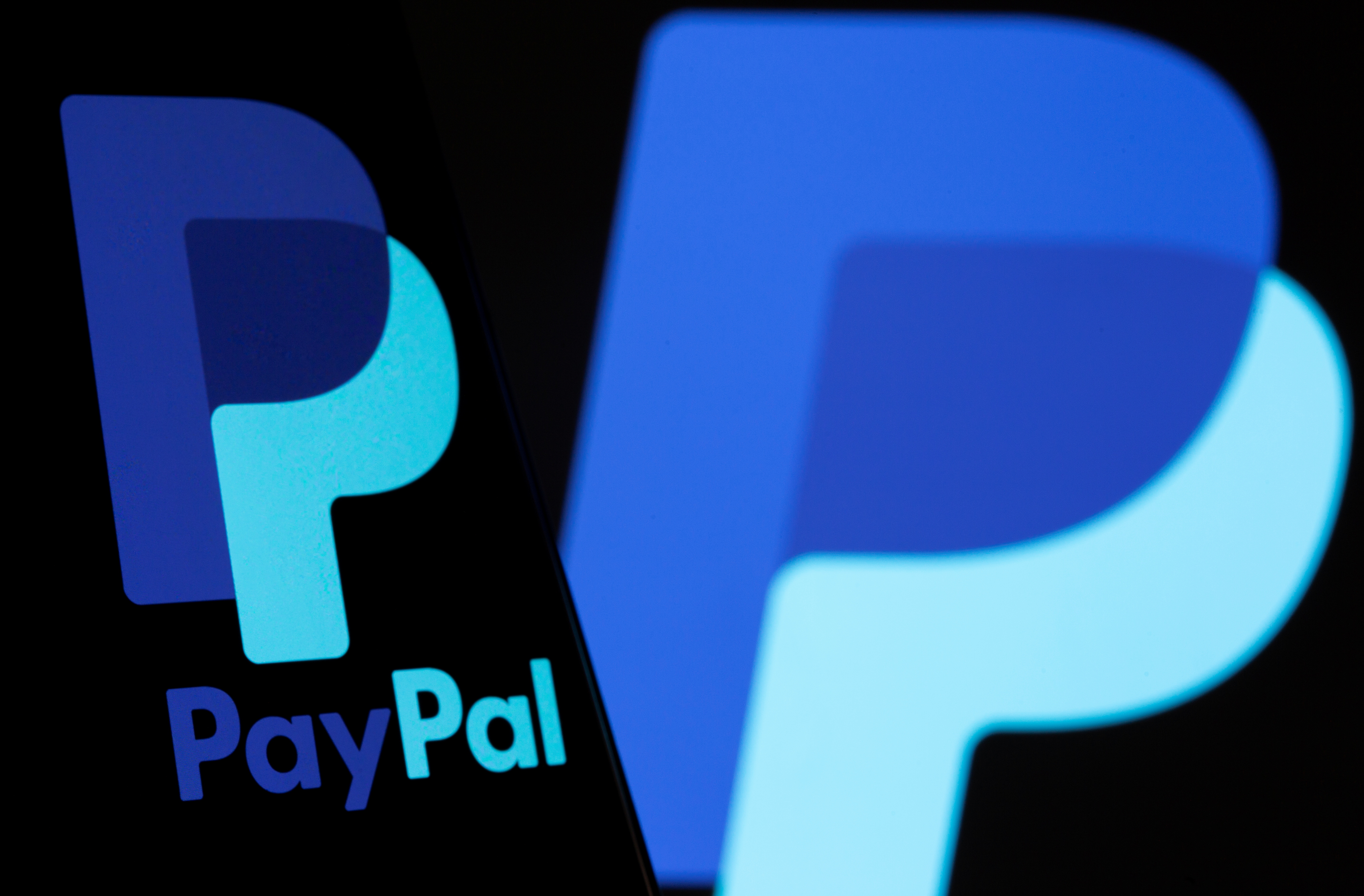 The PayPal logo is seen on a smartphone in front of the same logo shown in this illustration