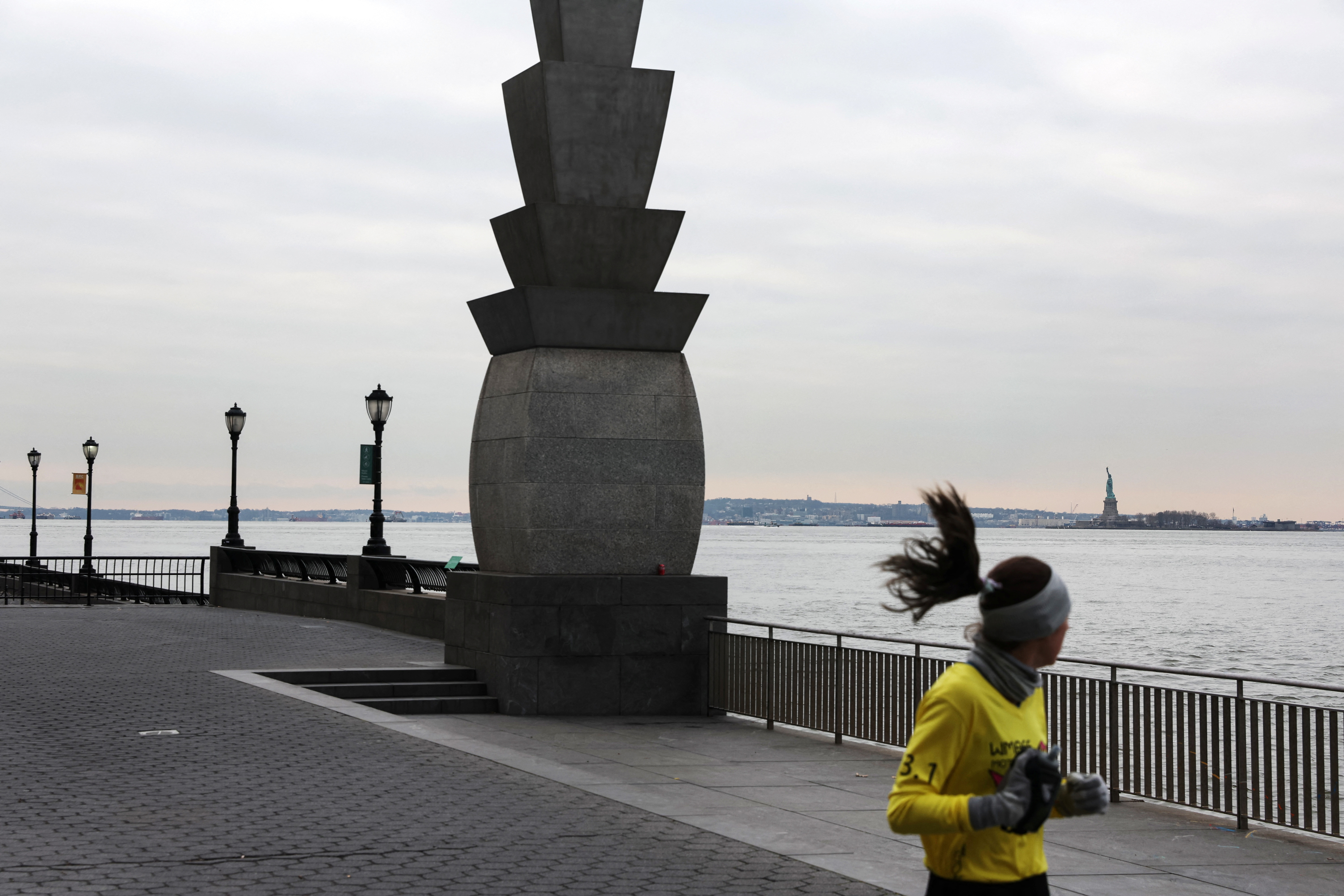 The Statue of Liberty stands on Liberty Island in New York Harbor as a woman jogs by in New York City