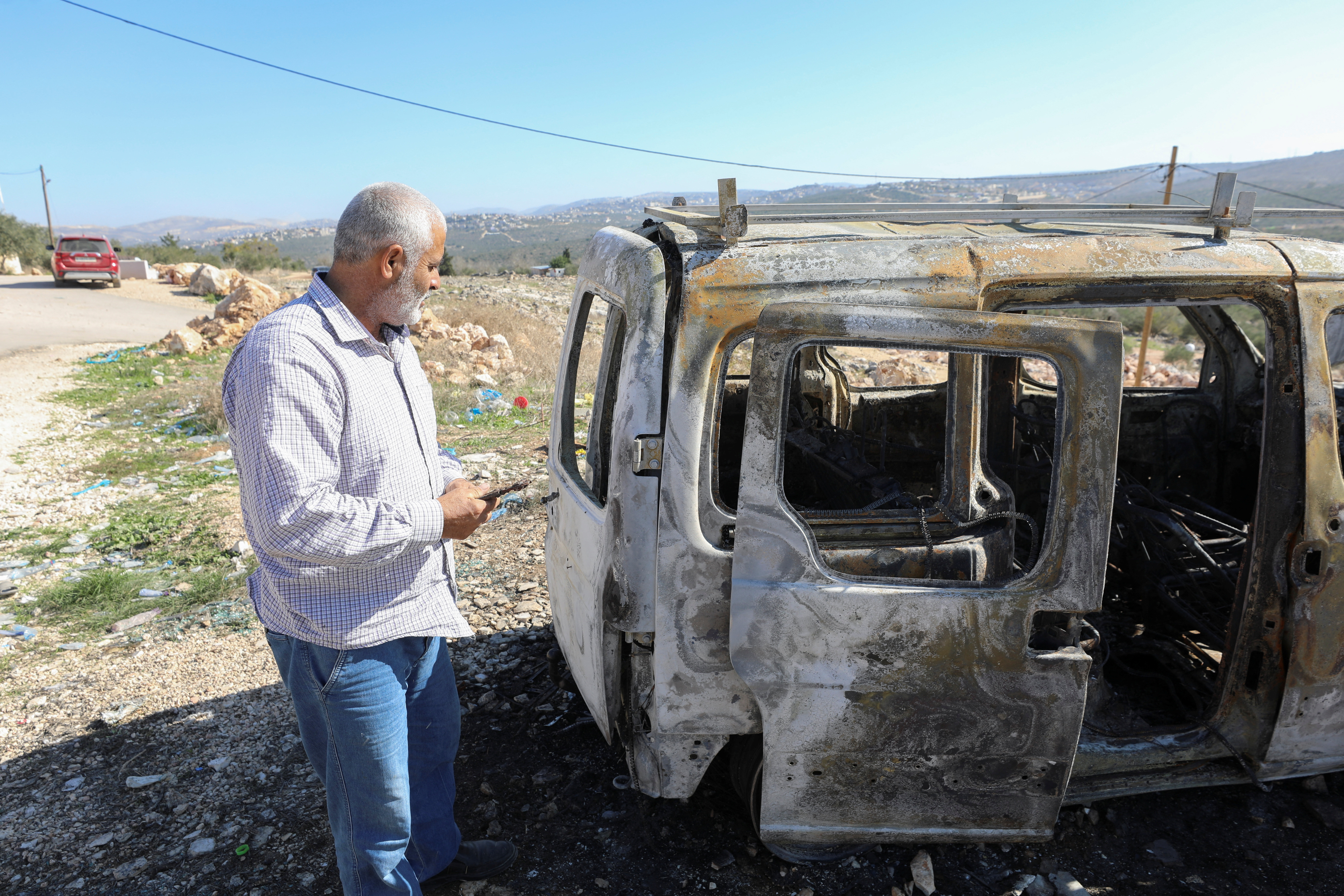 A Palestinian checks a car burned in Israeli settlers raid near Salfit in the West Bank