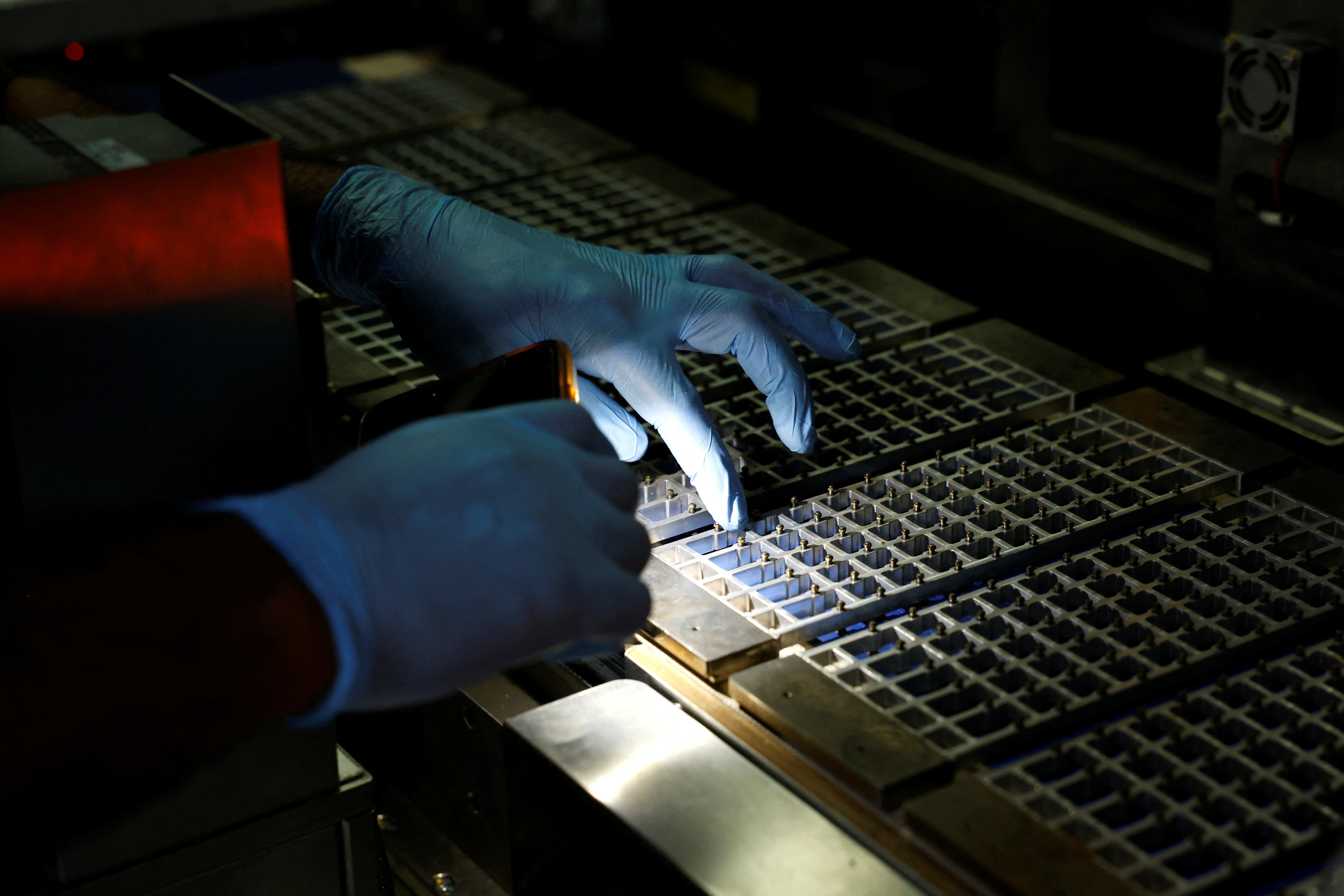 A technician checks the machine with a flashlight at a solar panel manufacturing hub, in Greater Noida