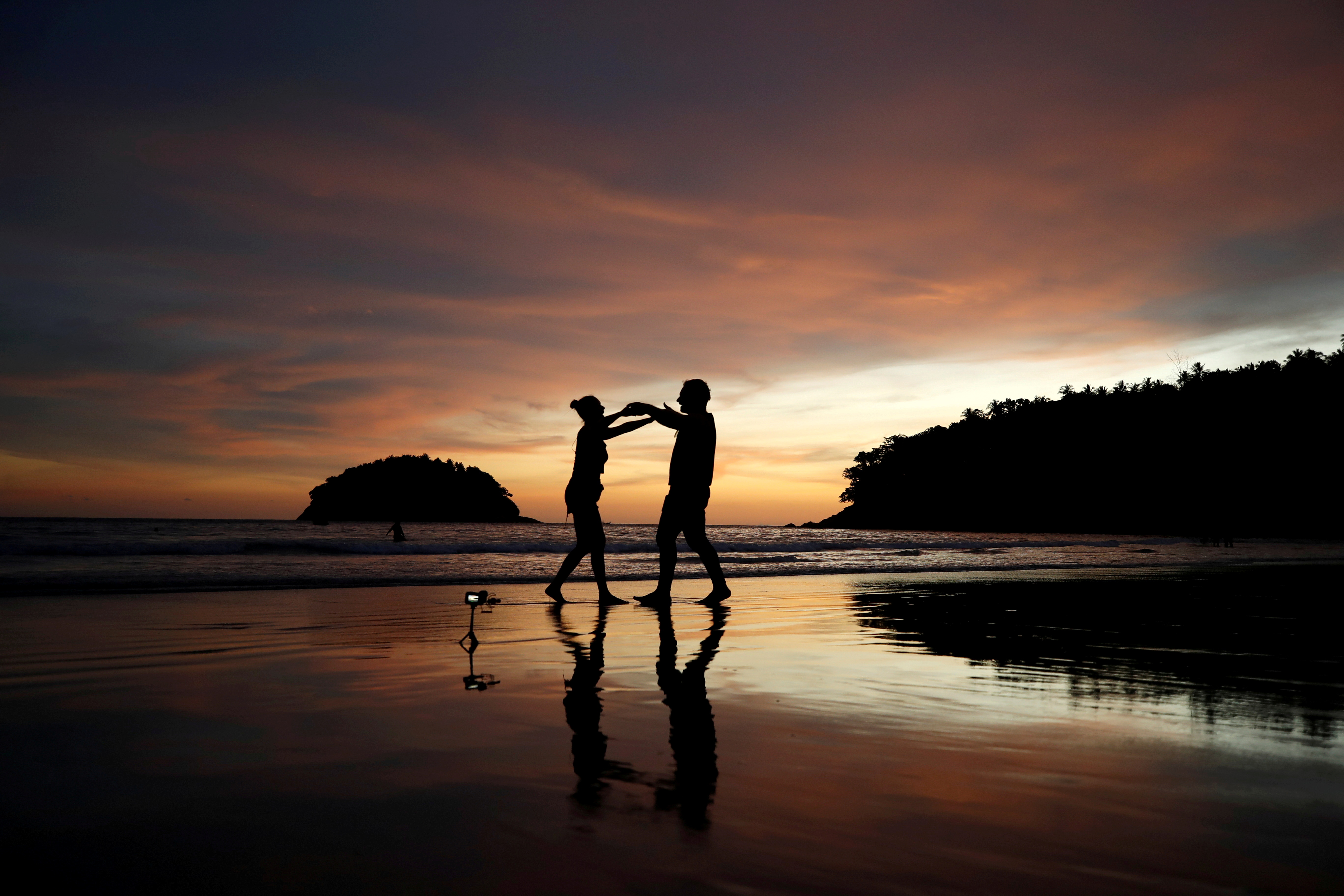 Local residents Stavros from Greece and Valina from Russia dance on an almost empty Kata beach as Phuket reopens to overseas tourists, allowing foreigners fully vaccinated against the coronavirus disease (COVID-19) to visit the resort island without quarantine, in Phuket, Thailand July 1, 2021. REUTERS/Jorge Silva/File Photo