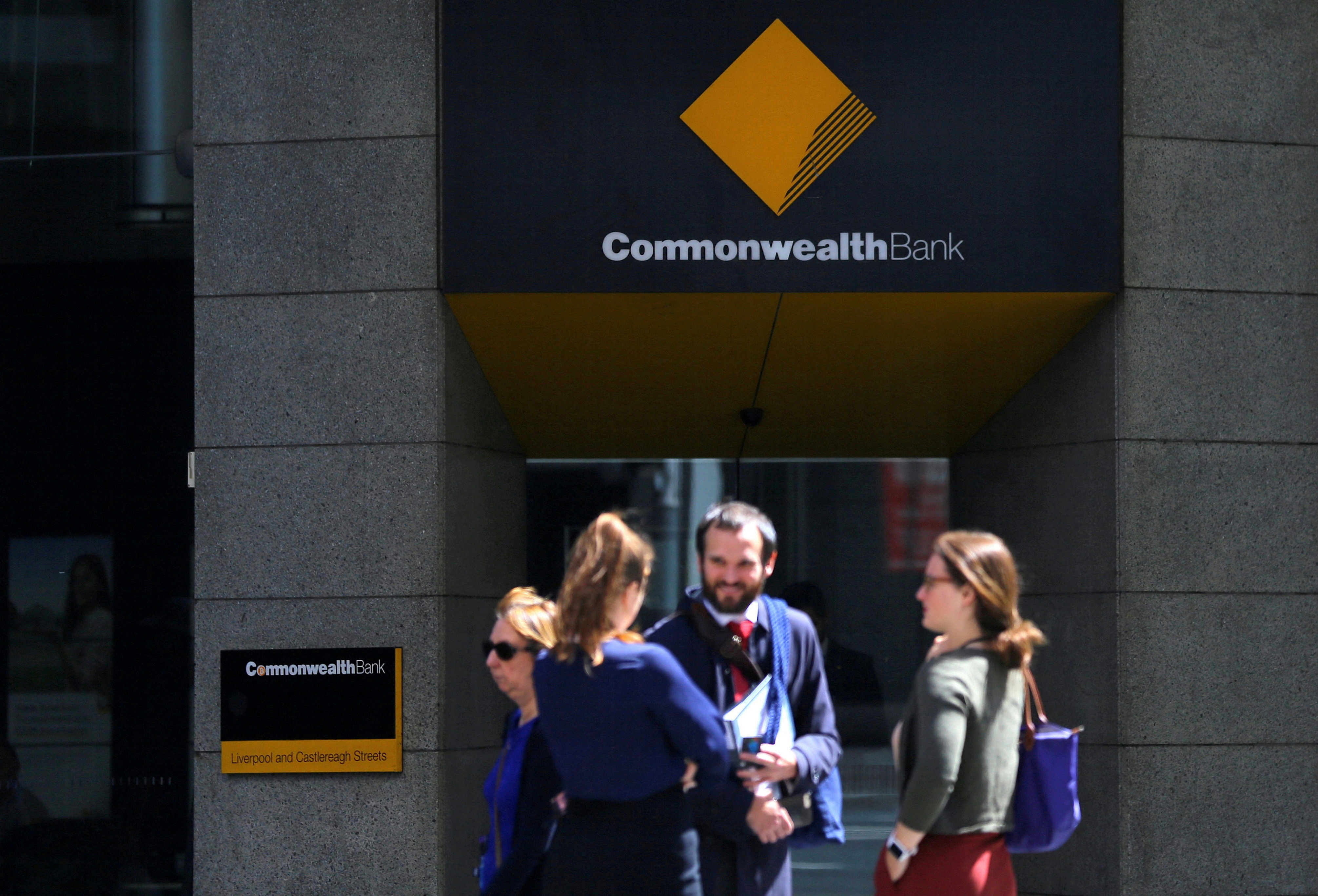 Pedestrians stand outside a branch of the Commonwealth Bank of Australia, Australia's biggest bank by market value, in central Sydney