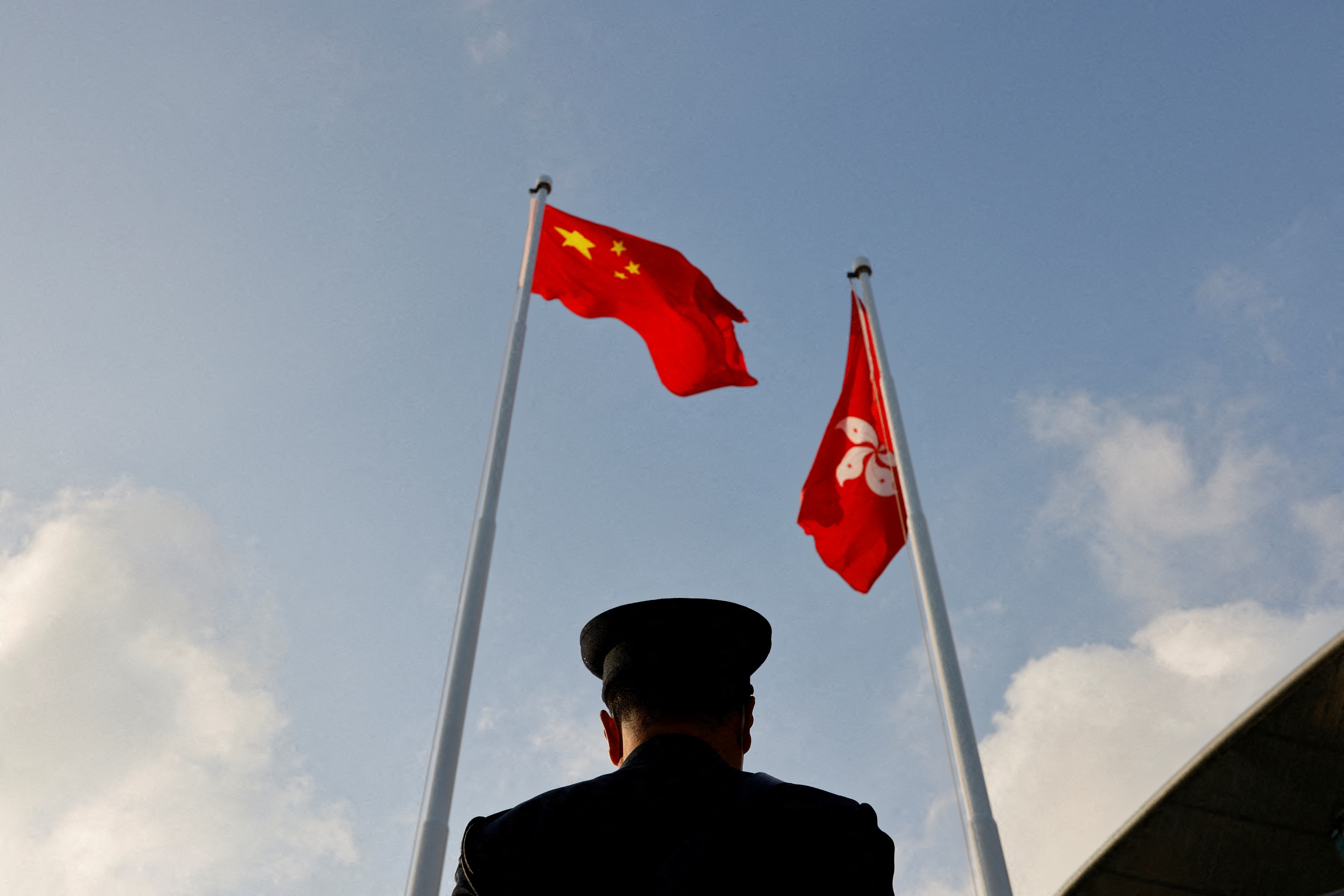 A police officer stands guard below China and Hong Kong flags during a flag raising ceremony, a week ahead of the Legislative Council election in Hong Kong