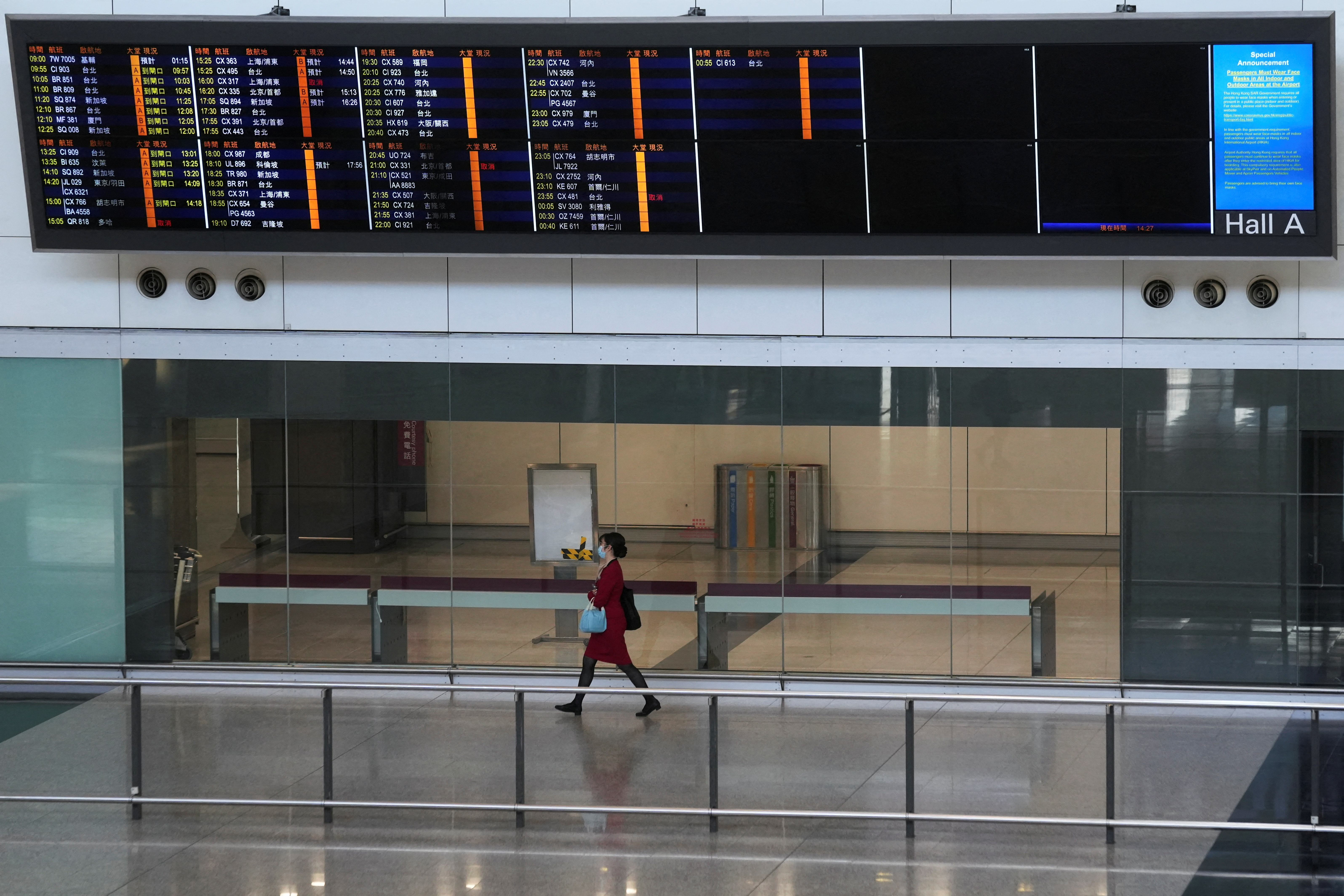A flight attendant walks under an information board at the arrivals hall of Hong Kong International Airport, following infections of the coronavirus disease (COVID-19) in Hong Kong, China January 11, 2022. REUTERS/Lam Yik