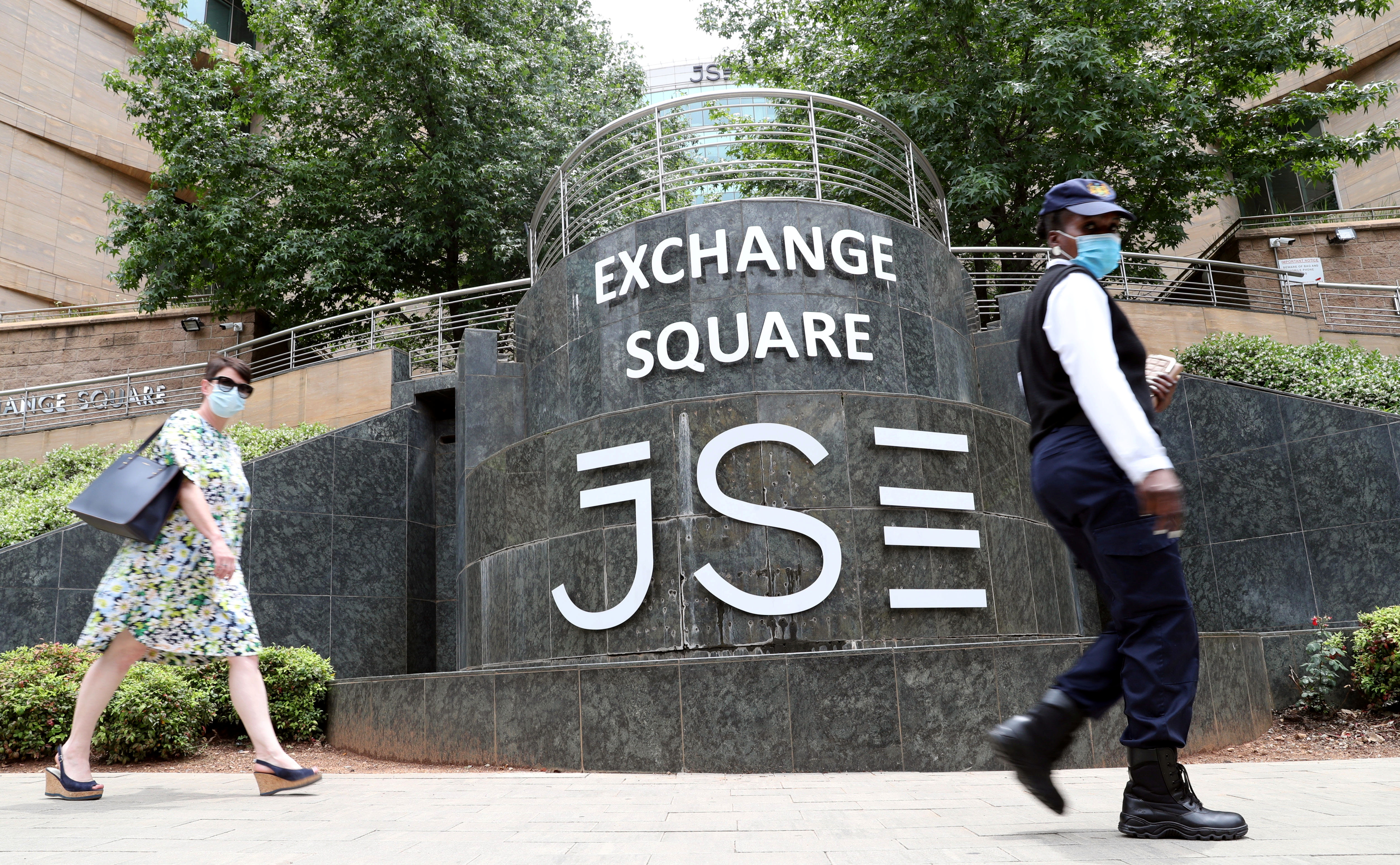 People wearing face masks walk past the Johannesburg Stock Exchange in Sandton