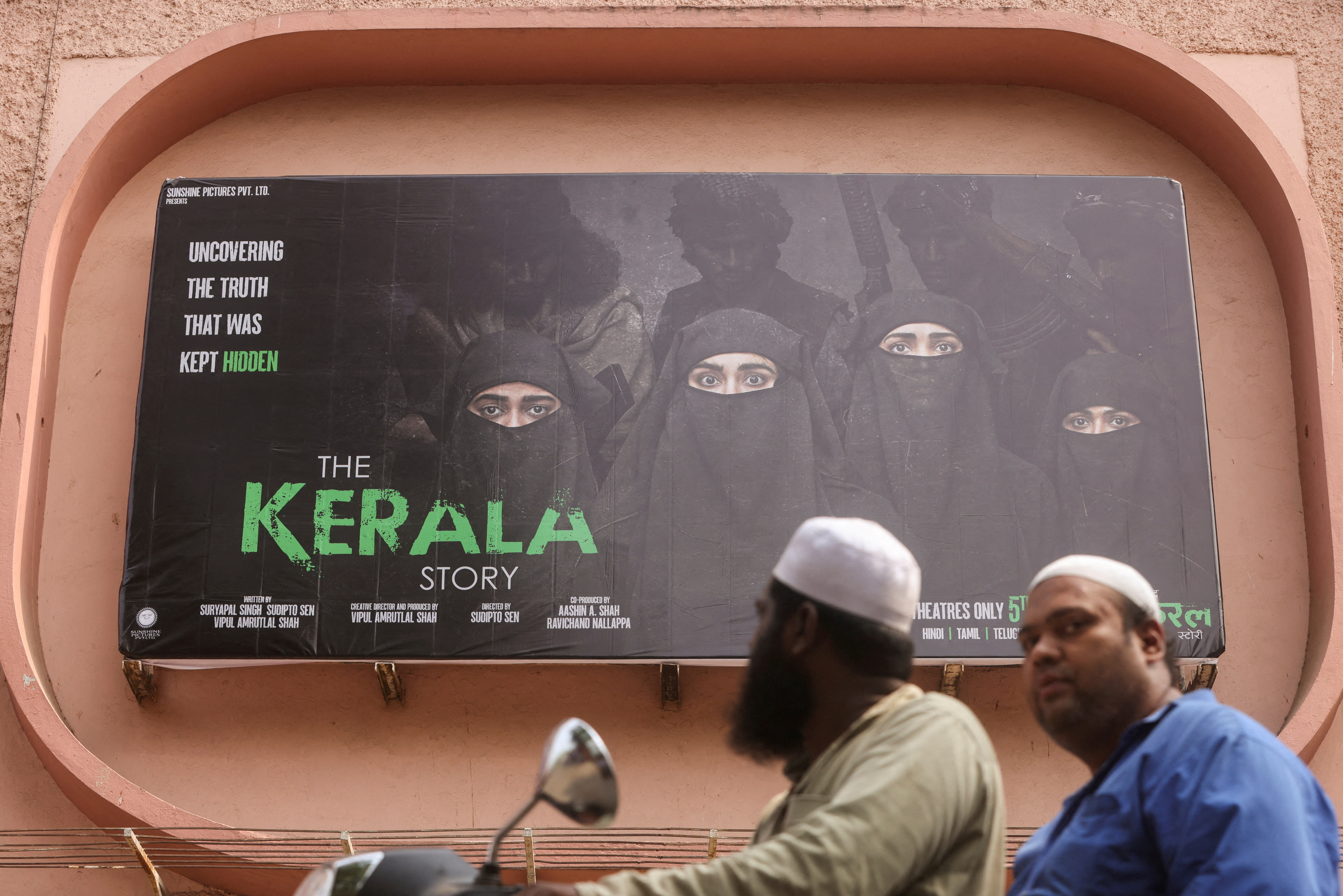 People ride past a poster of a Hindi movie titled "The Kerala Story", outside a cinema in Mumbai