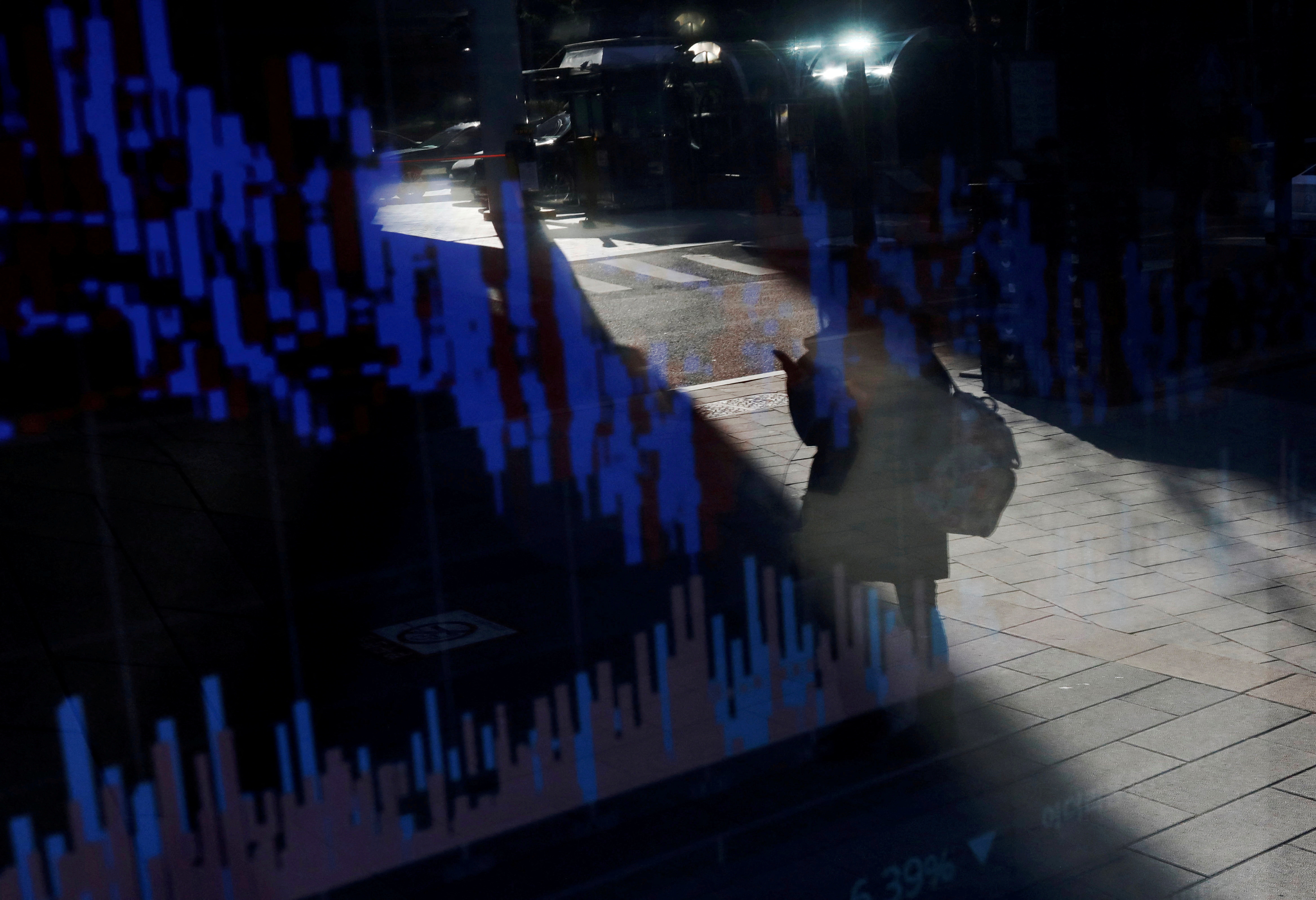 A woman using her mobile phone is reflected on an electric board showing exchange rates of various cryptocurrencies at Bithumb cryptocurrencies exchange in Seoul