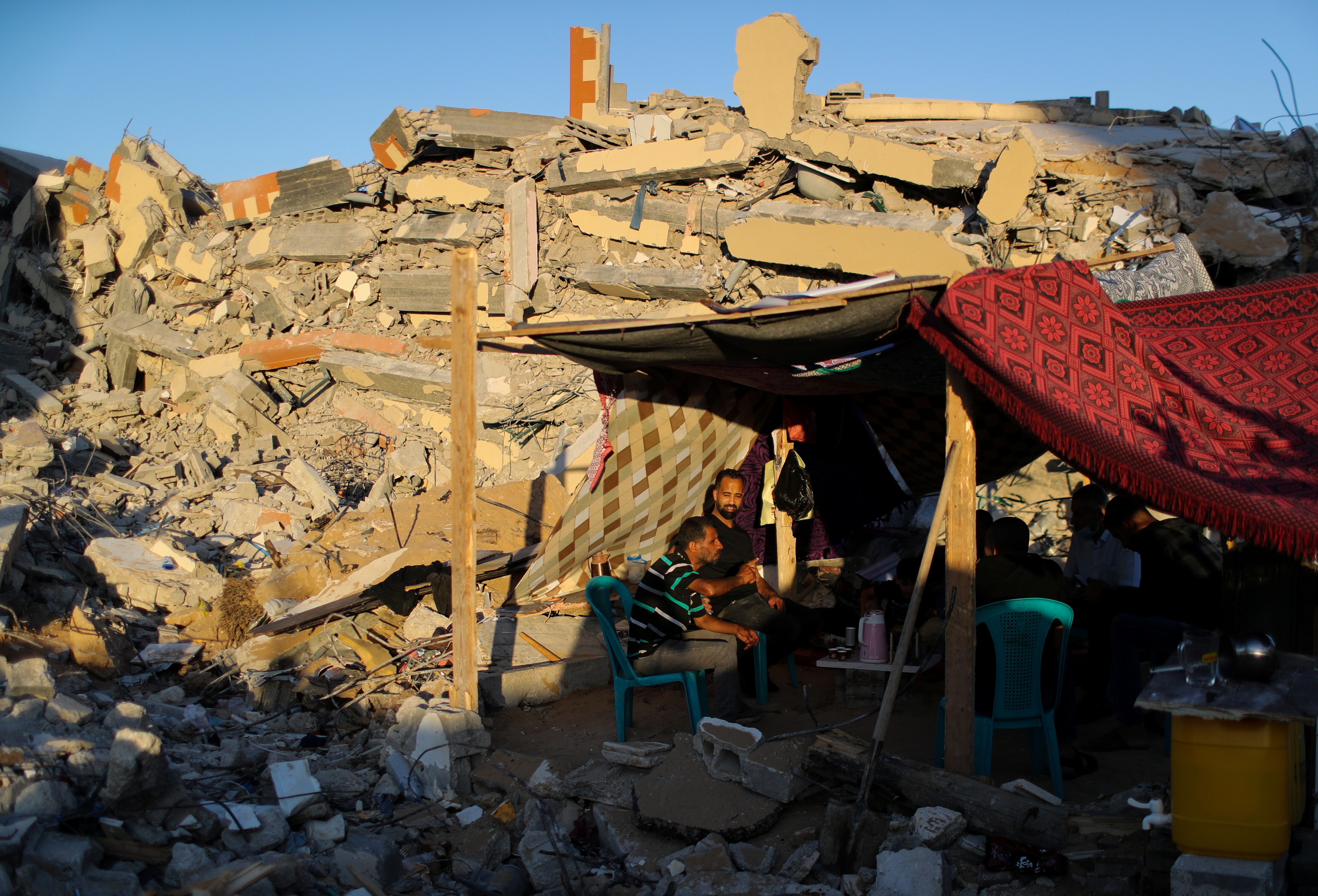 People sit near the rubble of their houses which were destroyed by Israeli air strikes during the Israel-Hamas fighting in Gaza Strip
