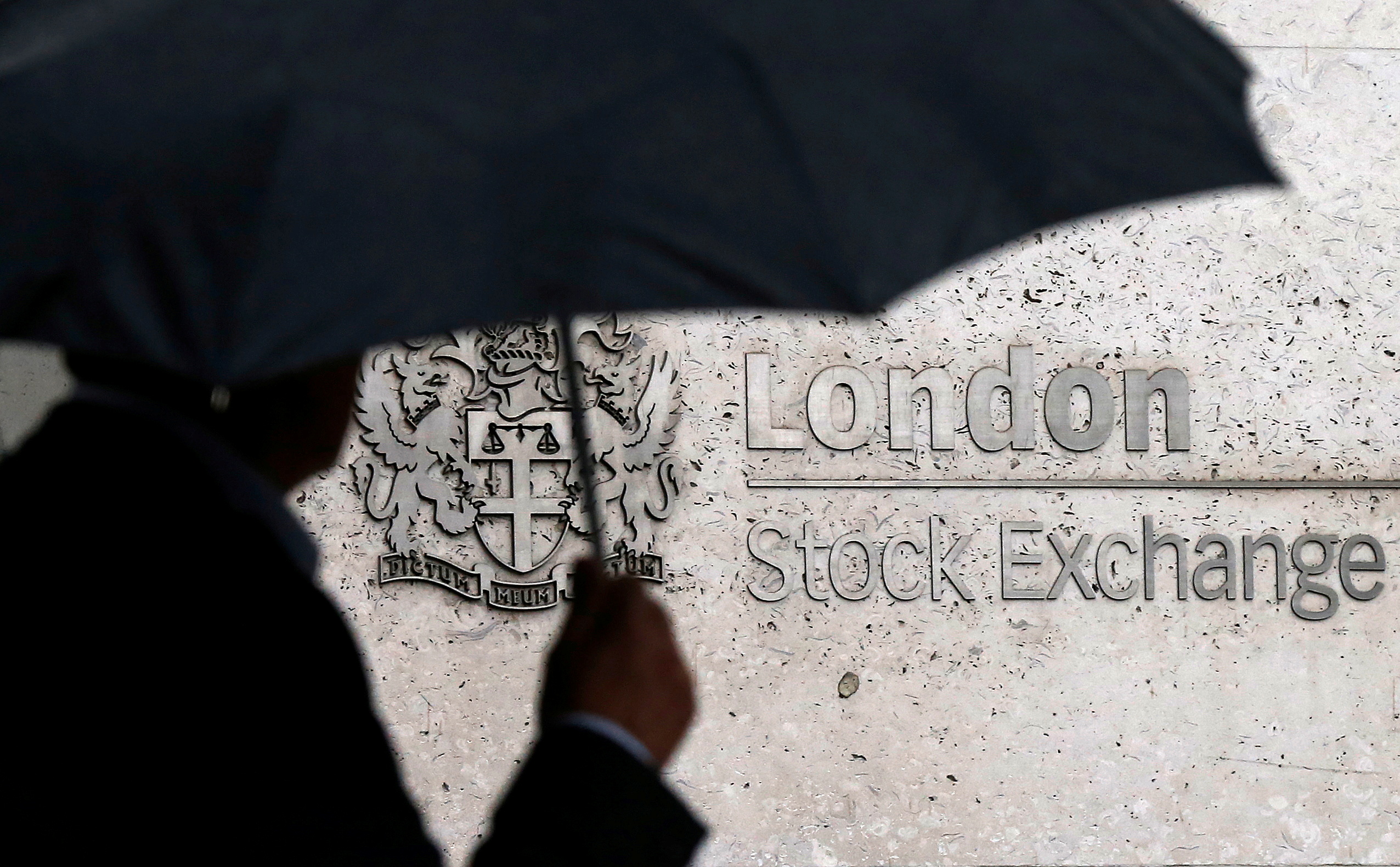 A man shelters under an umbrella as he walks past the London Stock Exchange in London, Britain, August 24, 2015. REUTERS/Suzanne Plunkett/File Photo/File Photo