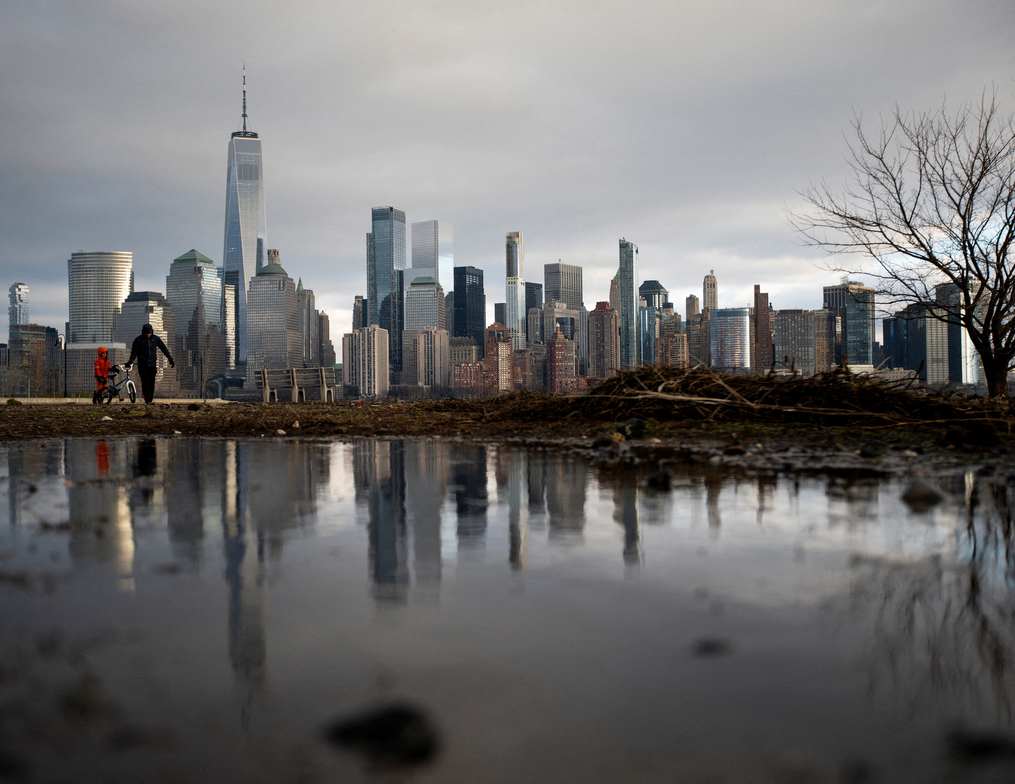 People walk near the shore in a local park in Jersey City, New Jersey, while storm clouds pass by the One World Trade Center in New York