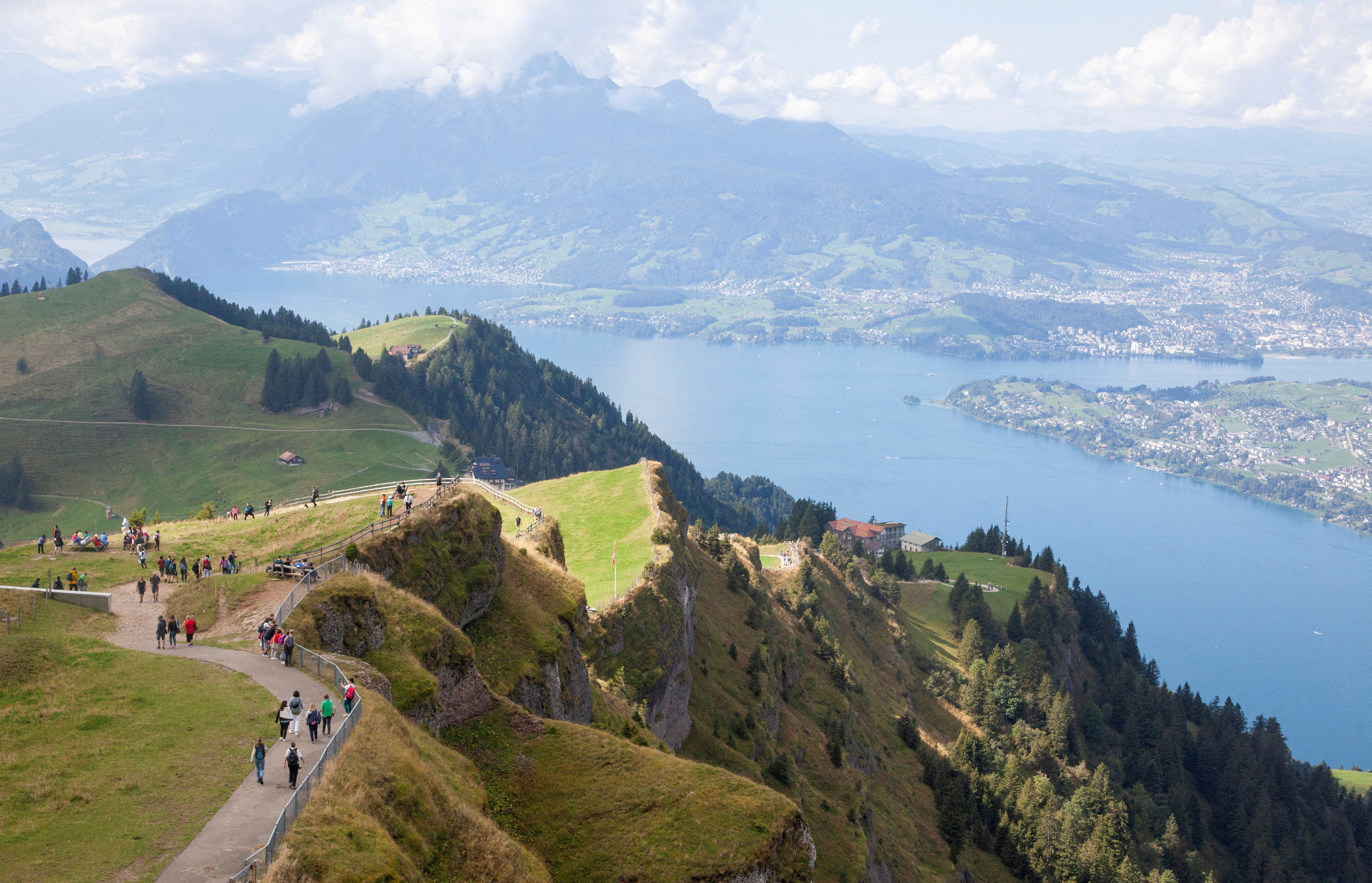 Tourists walk as Lake Lucerne is seen in the background, near the peak of Mount Rigi