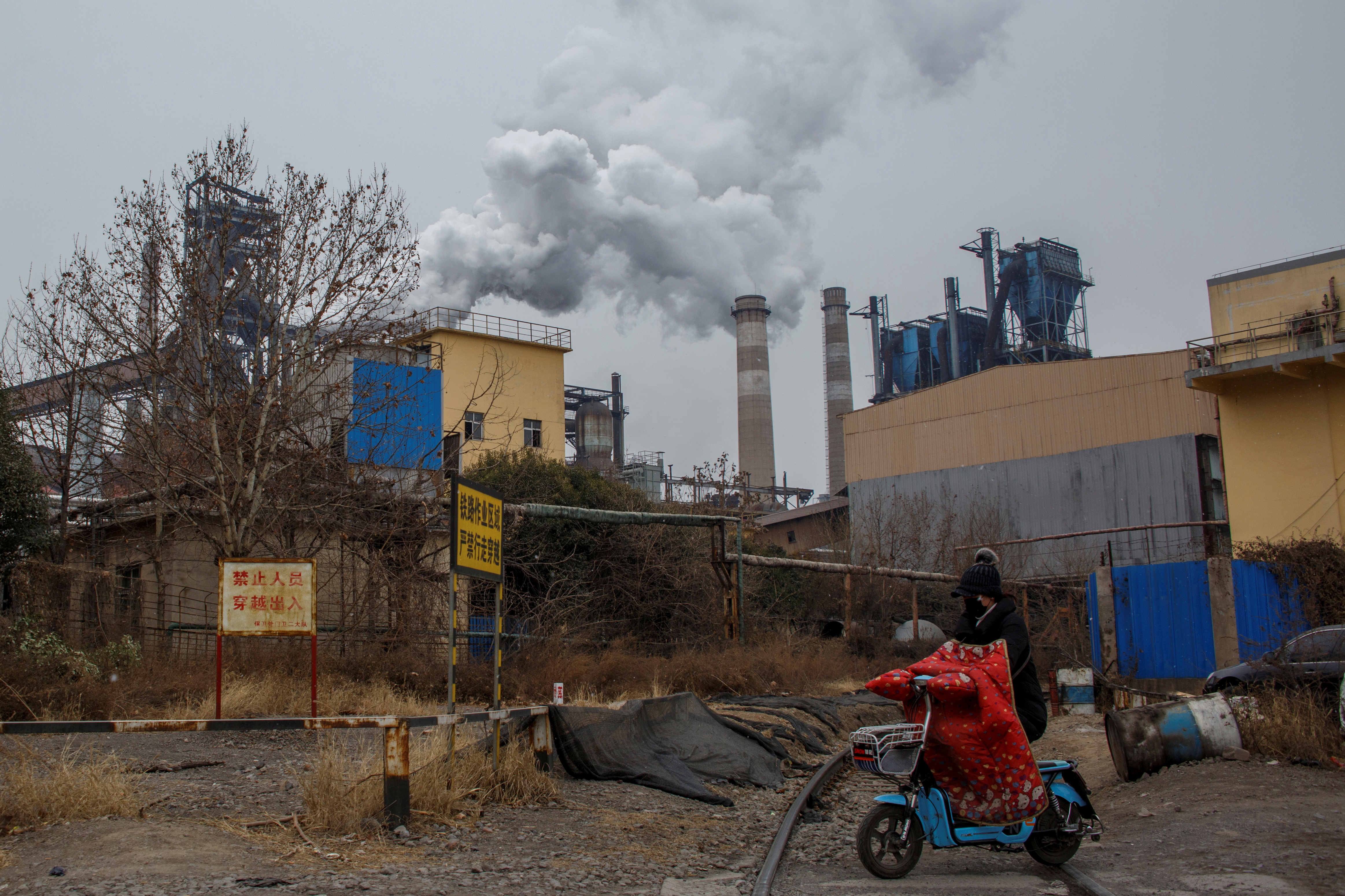 A woman rides a scooter past a steel plant in Anyang, Henan province, China, February 18, 2019. Picture taken February 18, 2019.  REUTERS/Thomas Peter
