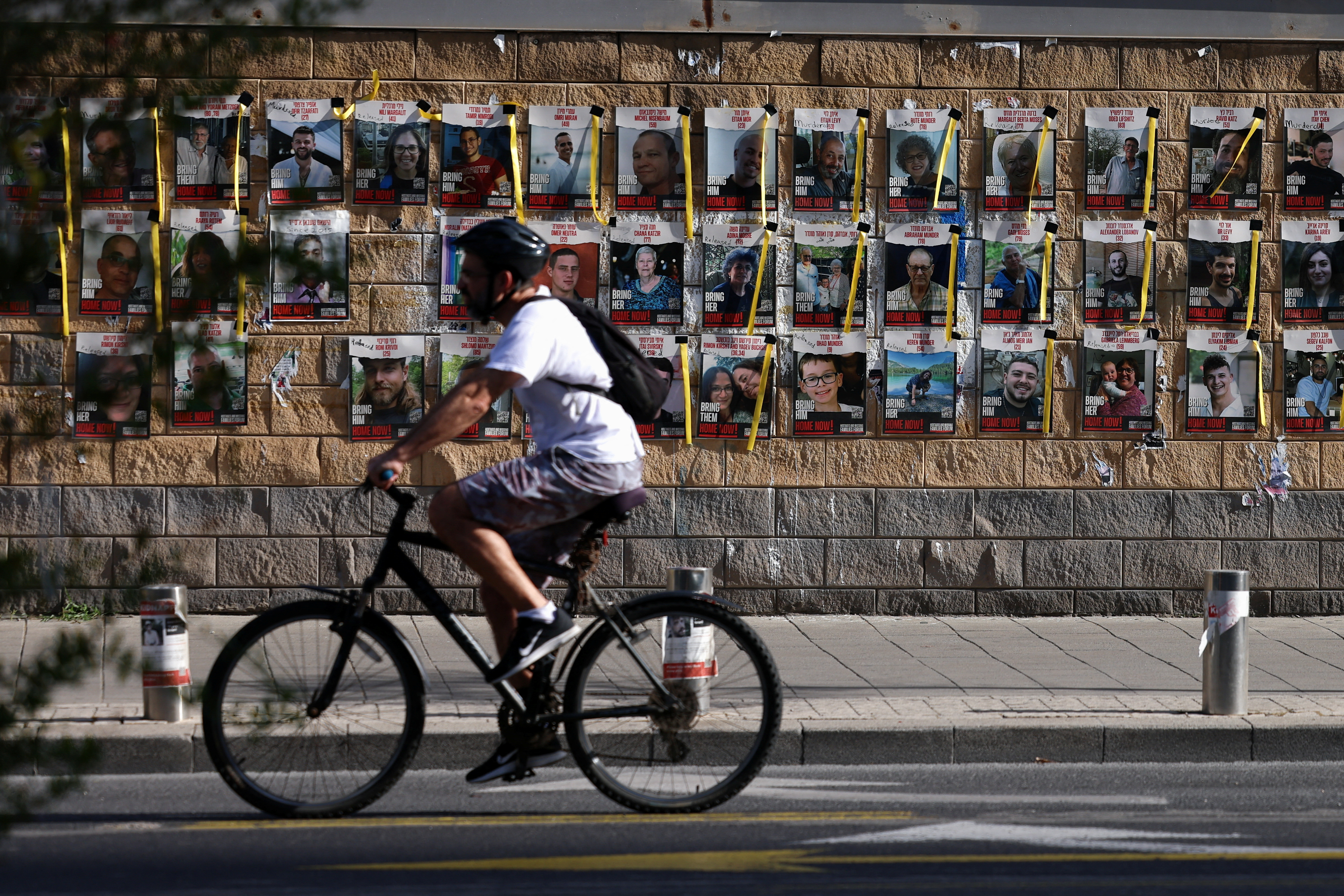 Man cycles past pictures of hostages kidnapped in October 7 attack on Israel by Hamas, in Tel Aviv