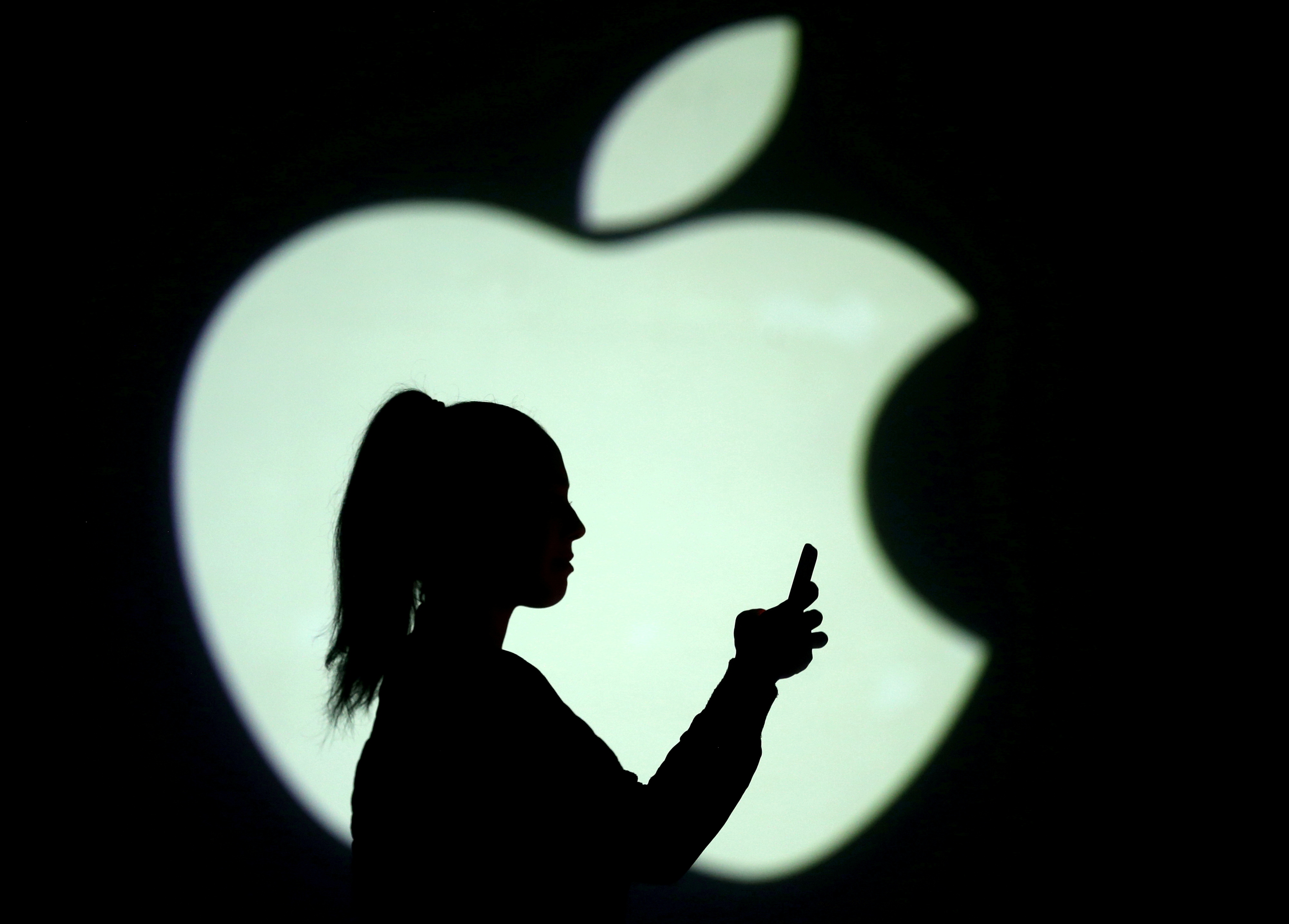 Silhouette of a mobile user seen next to a screen projection of the Apple logo in this picture illustration taken March 28, 2018.  REUTERS/Dado Ruvic/Illustration