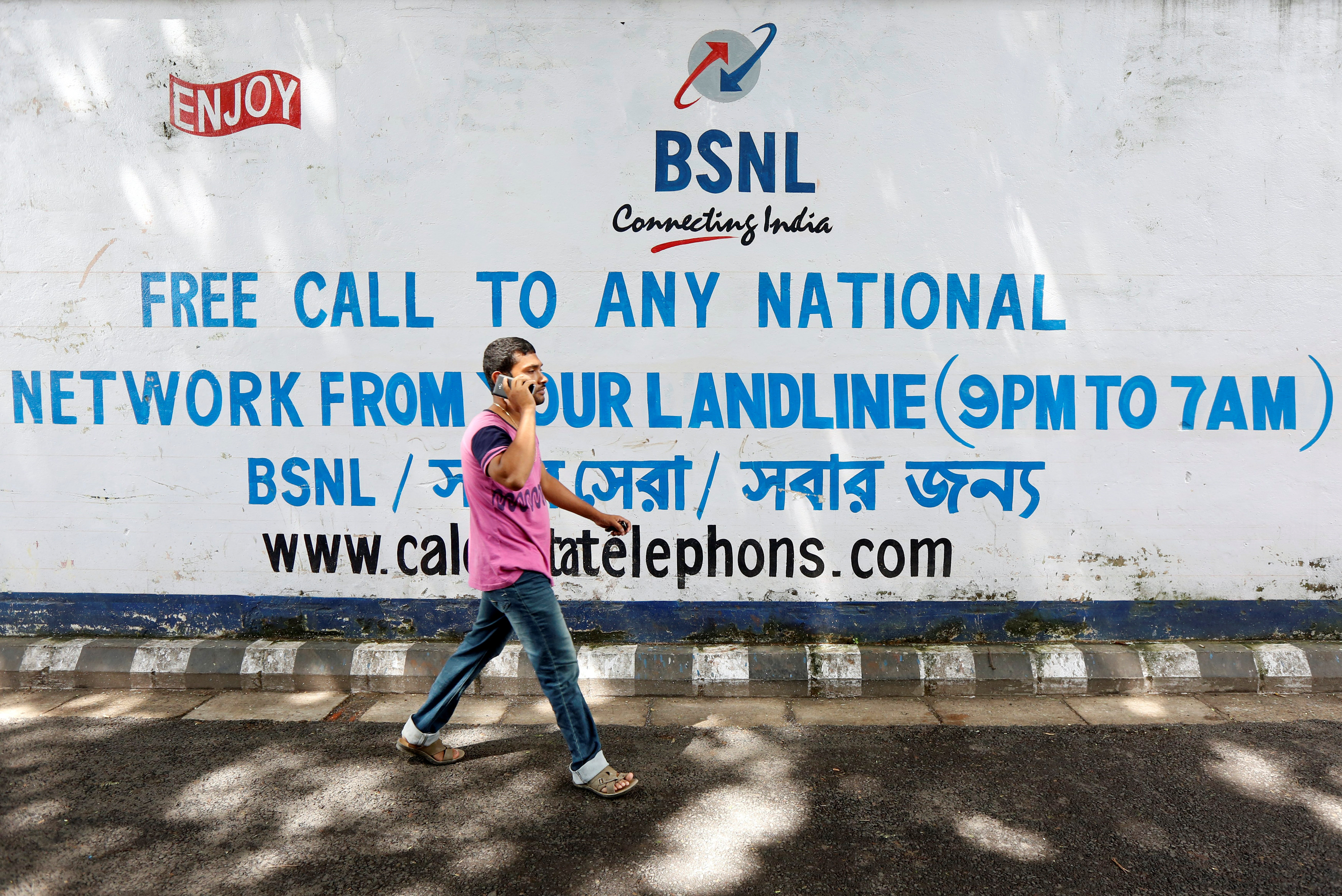 A man speaks on his mobile phone as he walks past a Bharat Sanchar Nigam Ltd advertisement painted on a wall outside its office in Kolkata