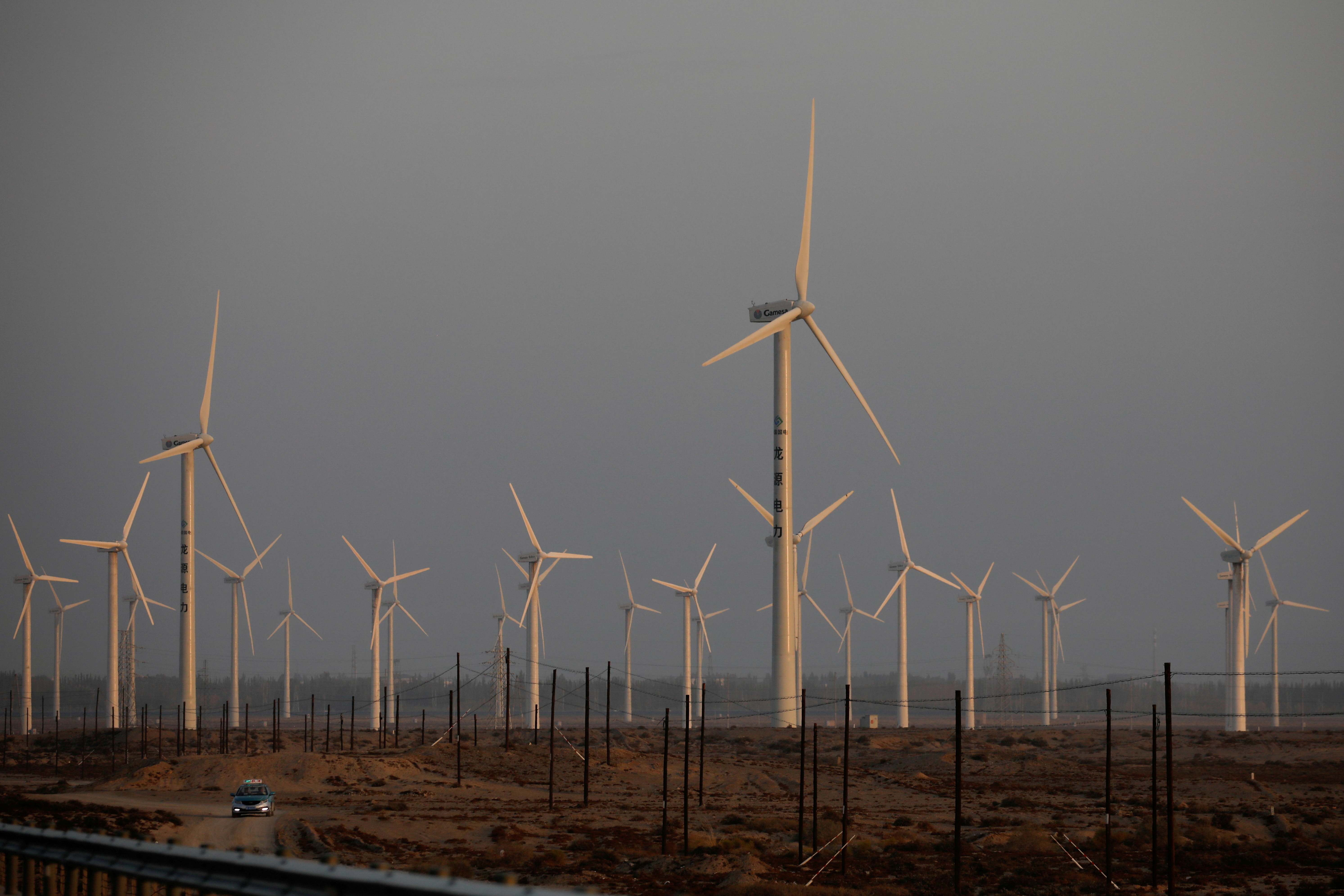 A car drives near wind turbines on a power station near Yumen