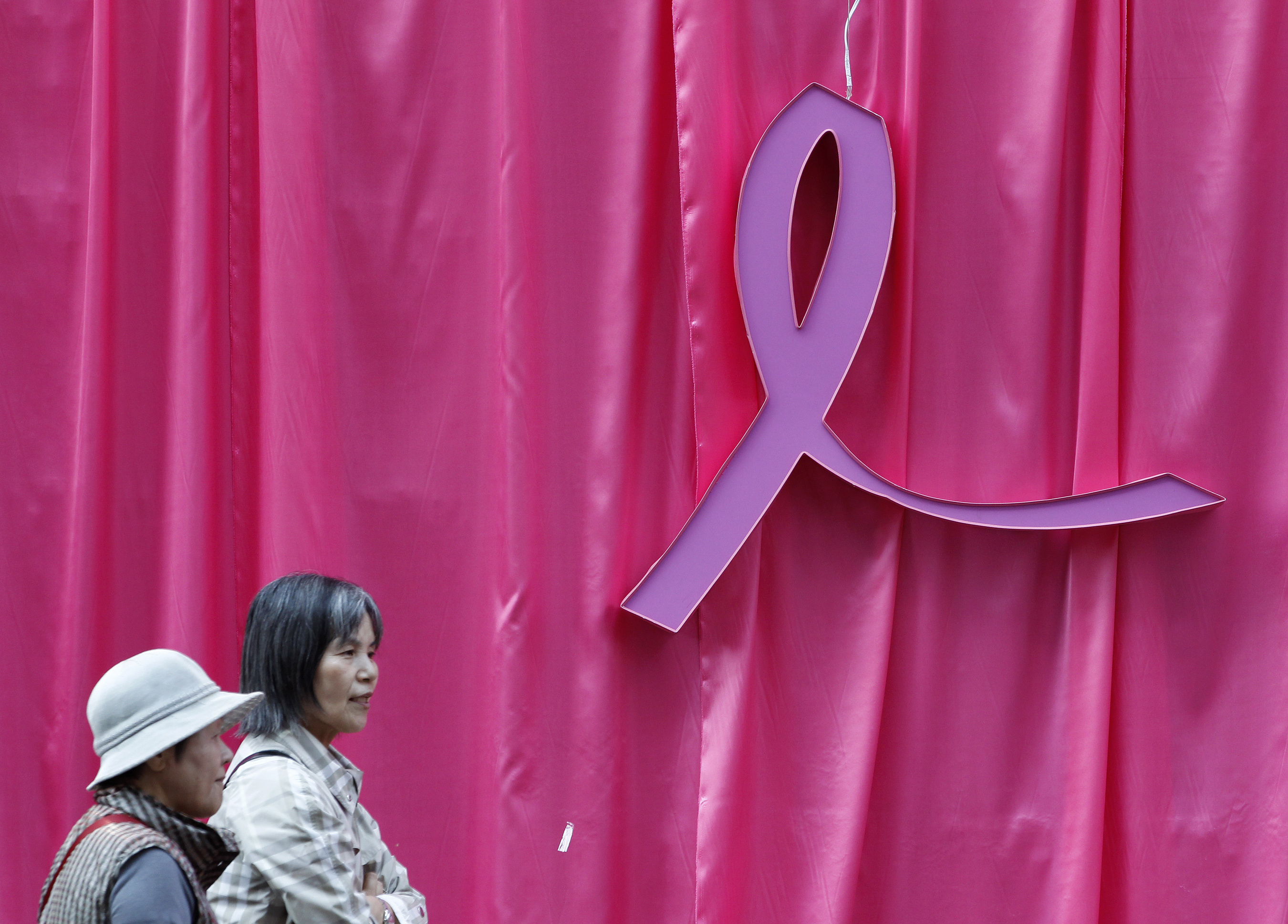 Visitors walk past a sculpture of a pink ribbon installed to promote the 