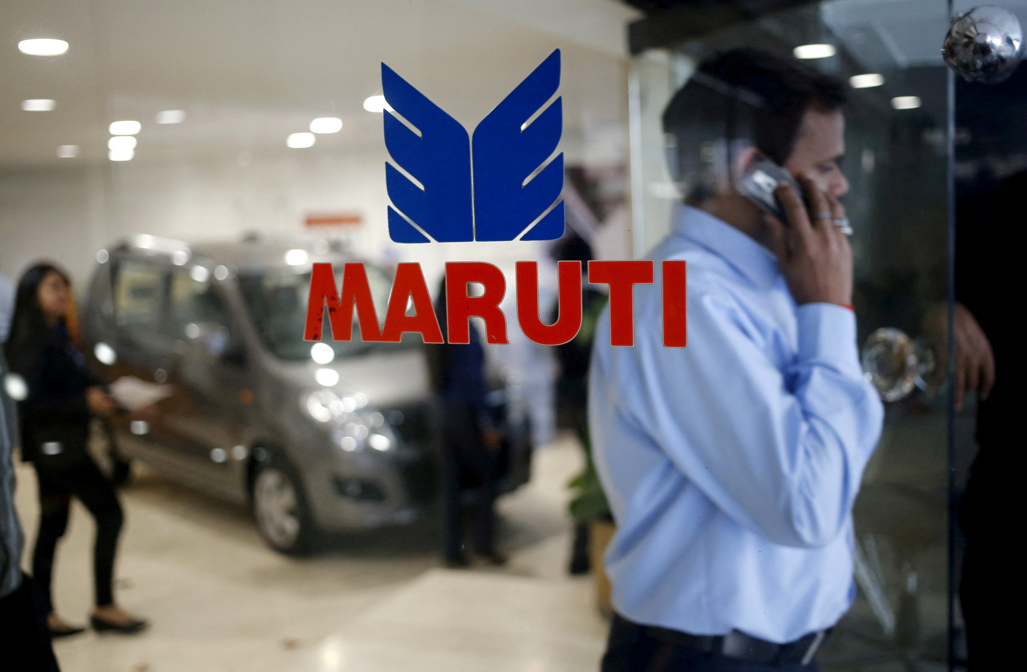 A man speaks on his mobile phone as he exits a glass door with the logo of  Maruti Suzuki India Limited at a showroom in New Delhi,
