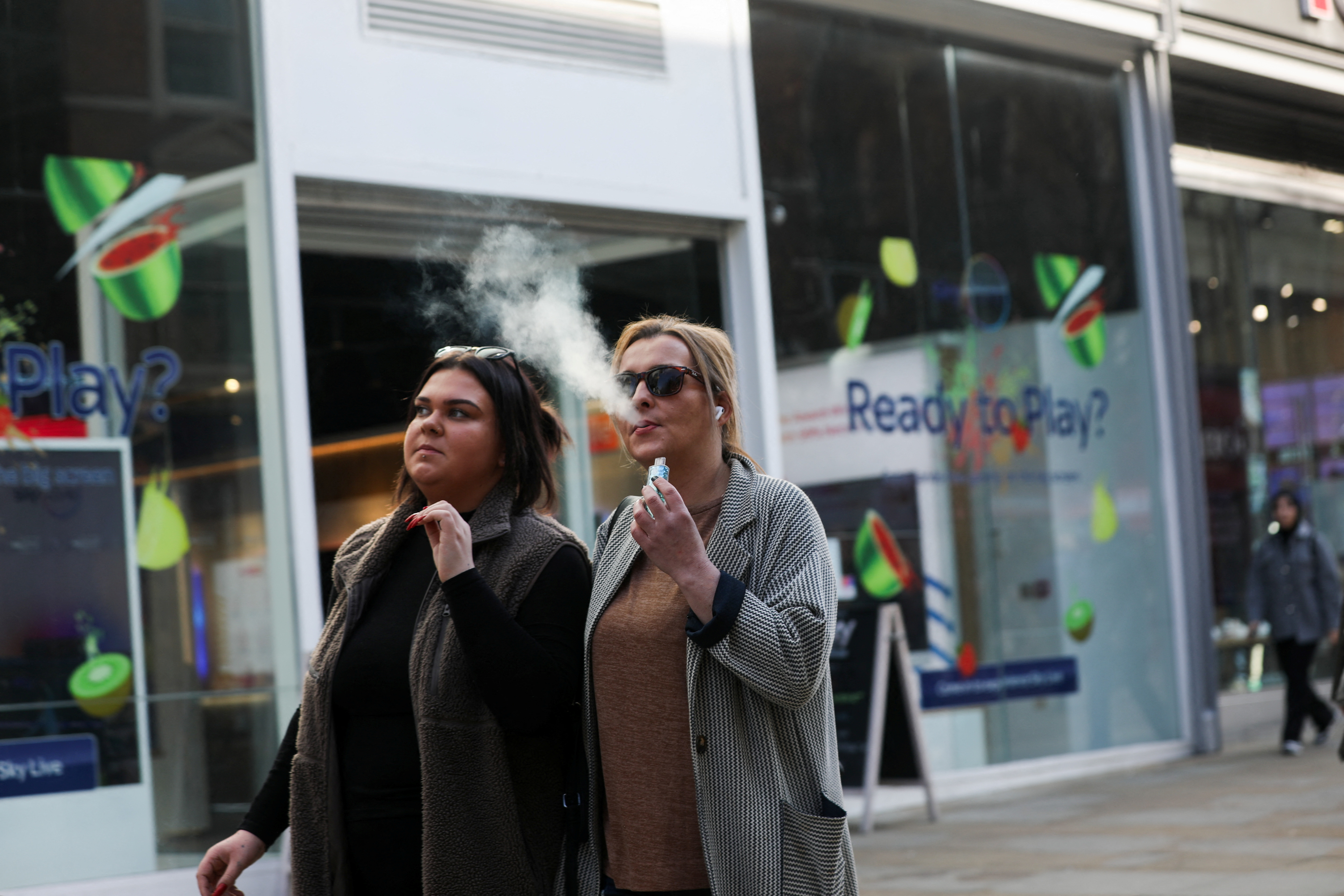 A woman holds an e-cigarette as she vapes on a street in Manchester