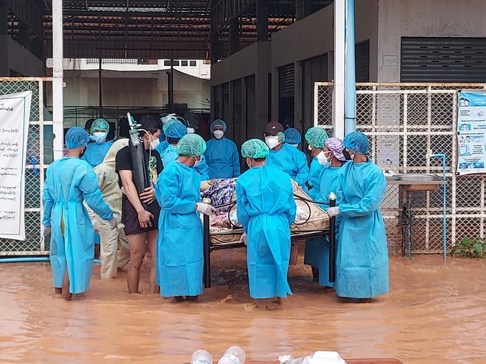 Volunteers in protective suits carry a COVID-19 patient lying on a hospital bed following floods, in Myawaddy