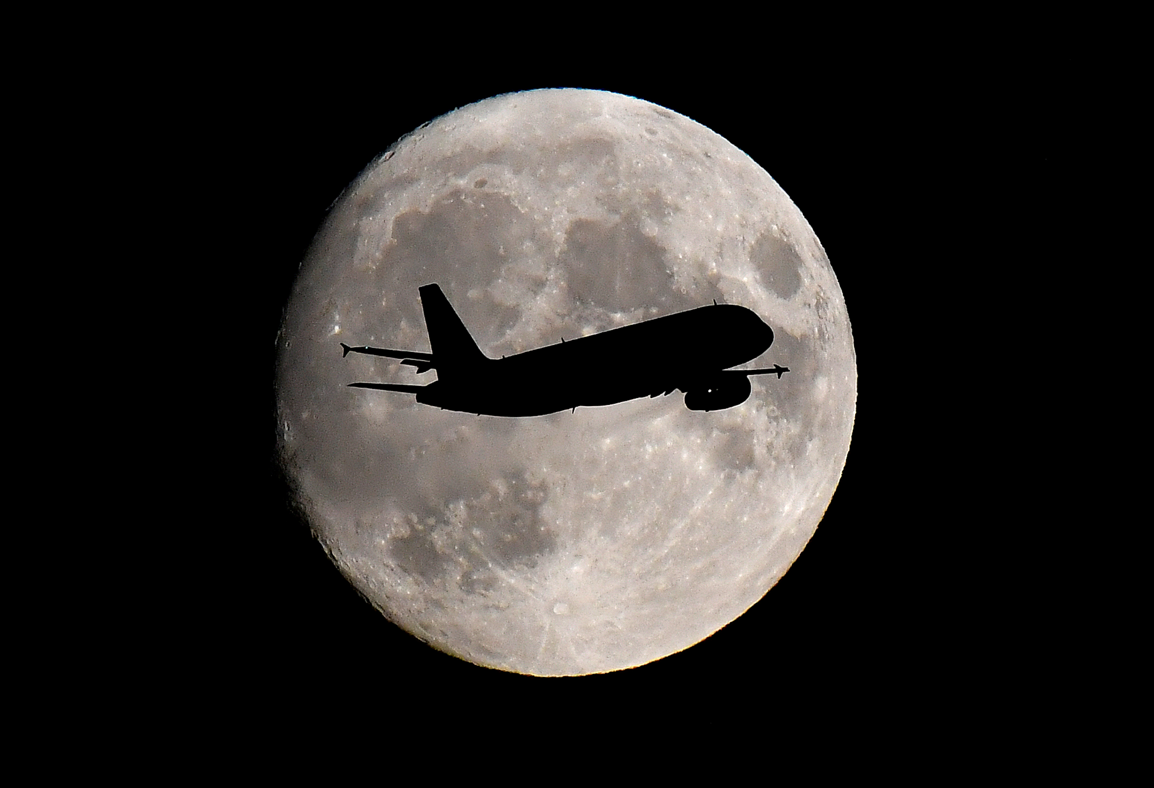 A passenger plane passes in front of the moon as it makes its final landing approach to Heathrow Airport in London