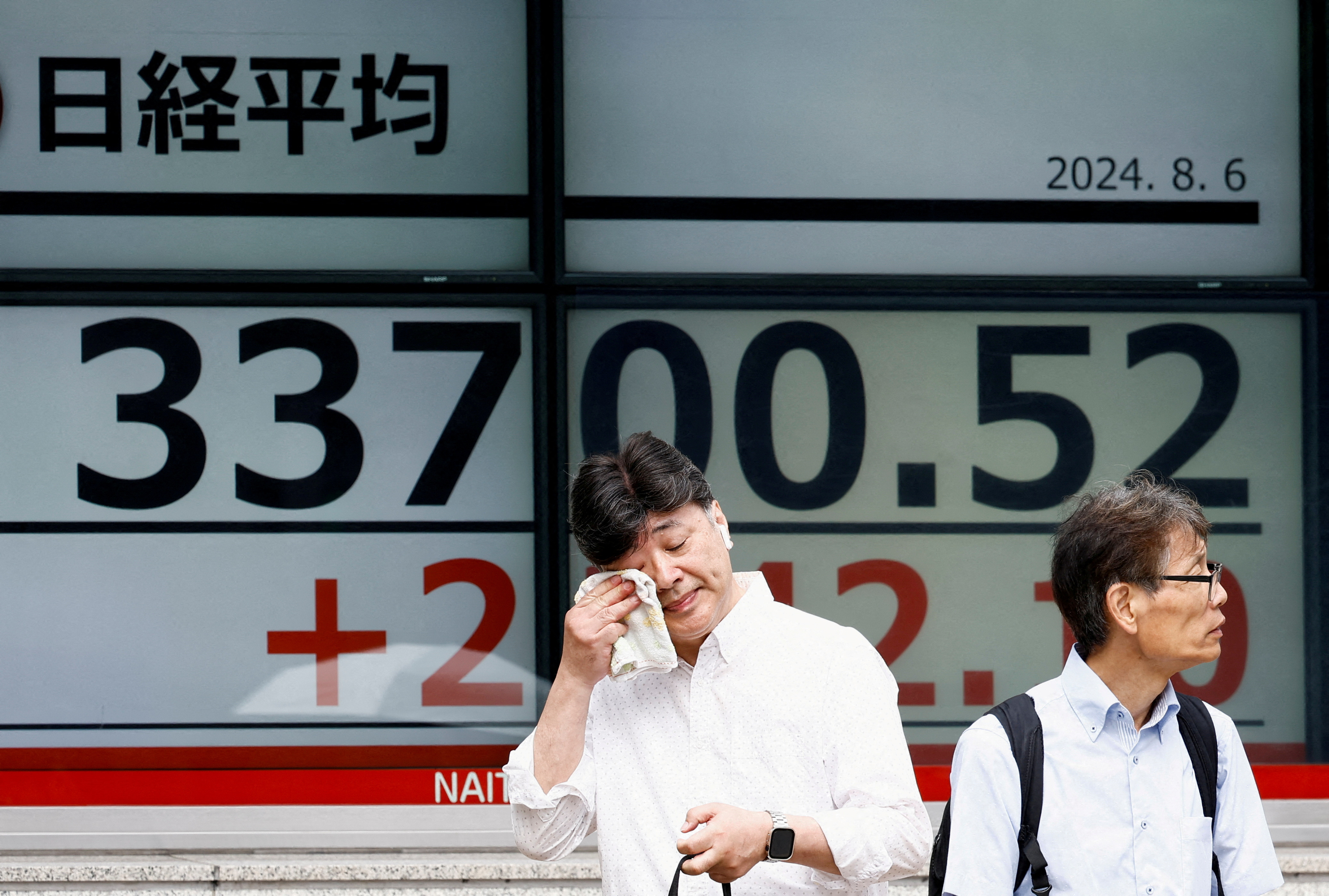 A passerby gestures in front of an electronic board displaying the Nikkei stock average outside a brokerage in Tokyo