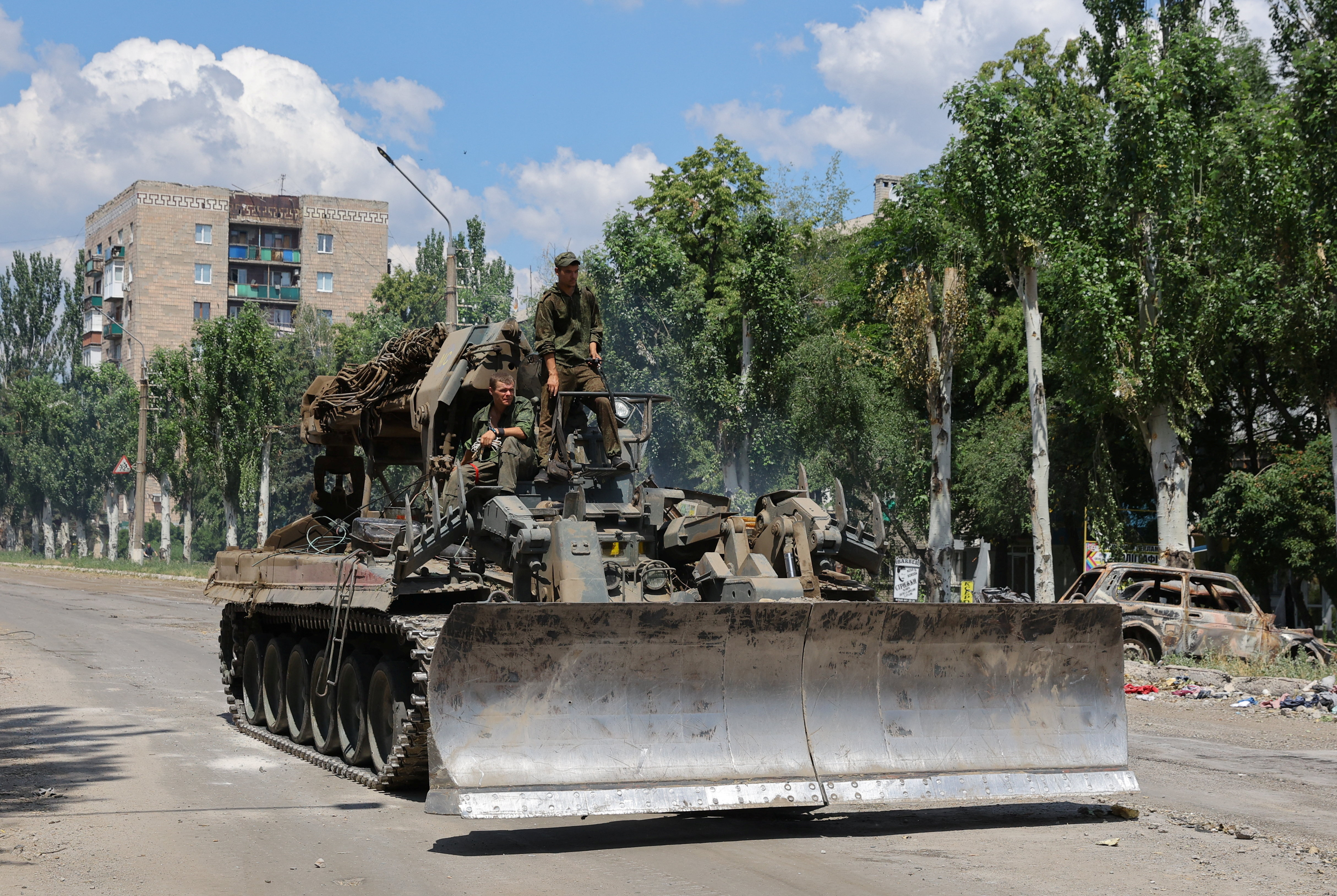 Service members of pro-Russian troops ride on top of a combat engineering vehicle in Lysychansk