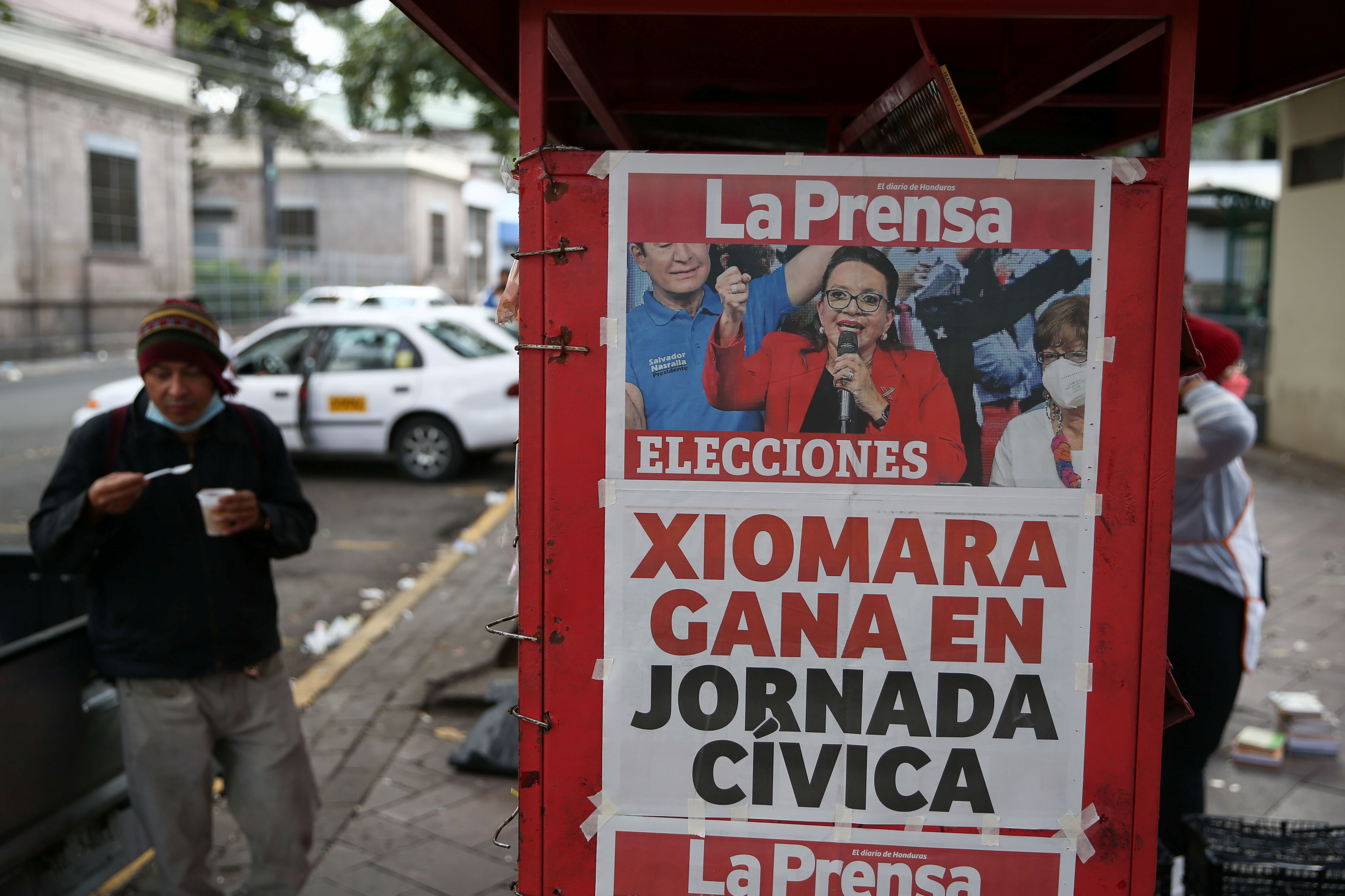A man eats by a newspaper stand that displays a cover story on the preliminary results of the general election in Tegucigalpa, Honduras, November 29, 2021. REUTERS/Jose Cabezas