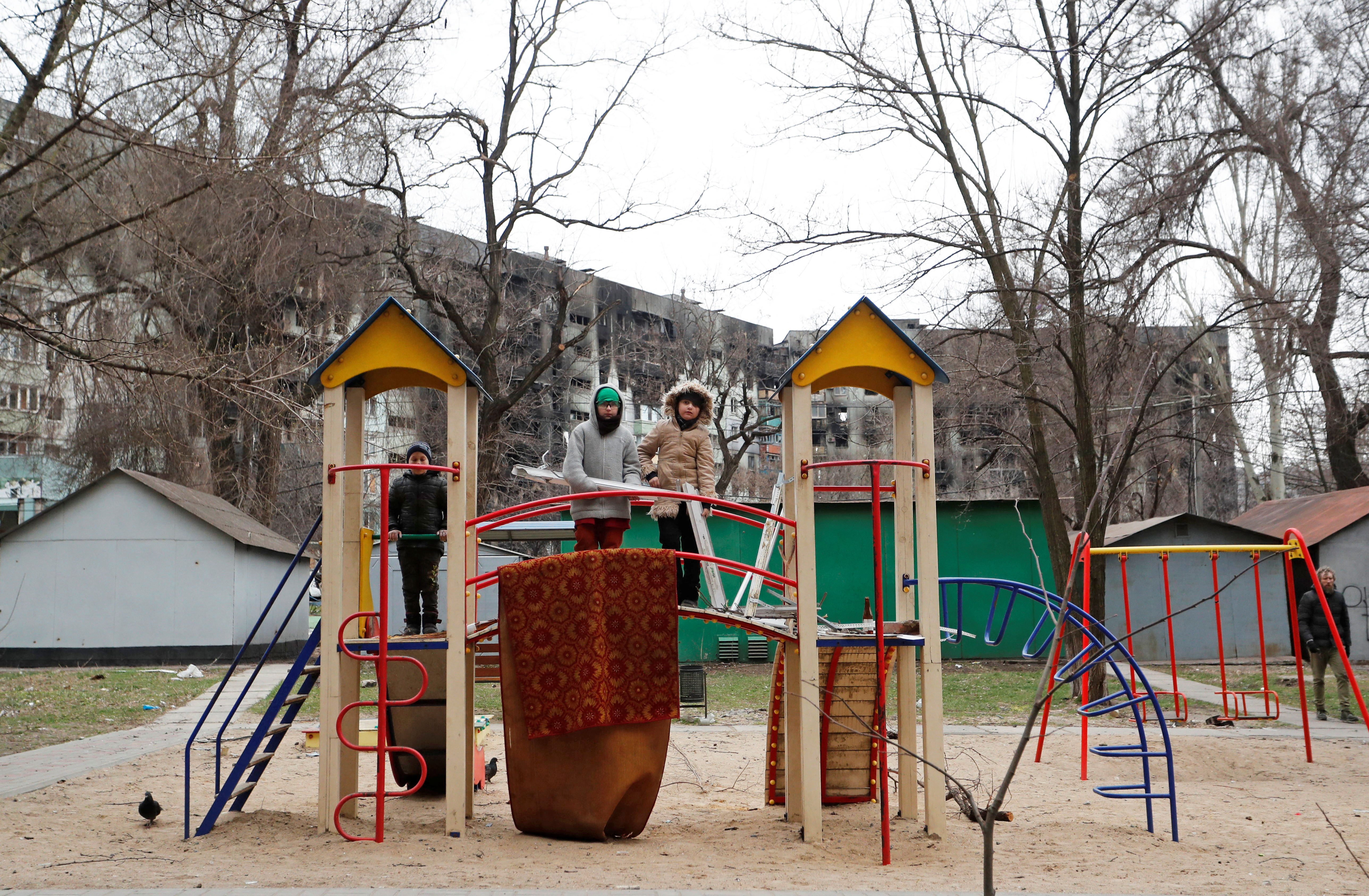 Children play at the playground near a damaged apartment building in Mariupol