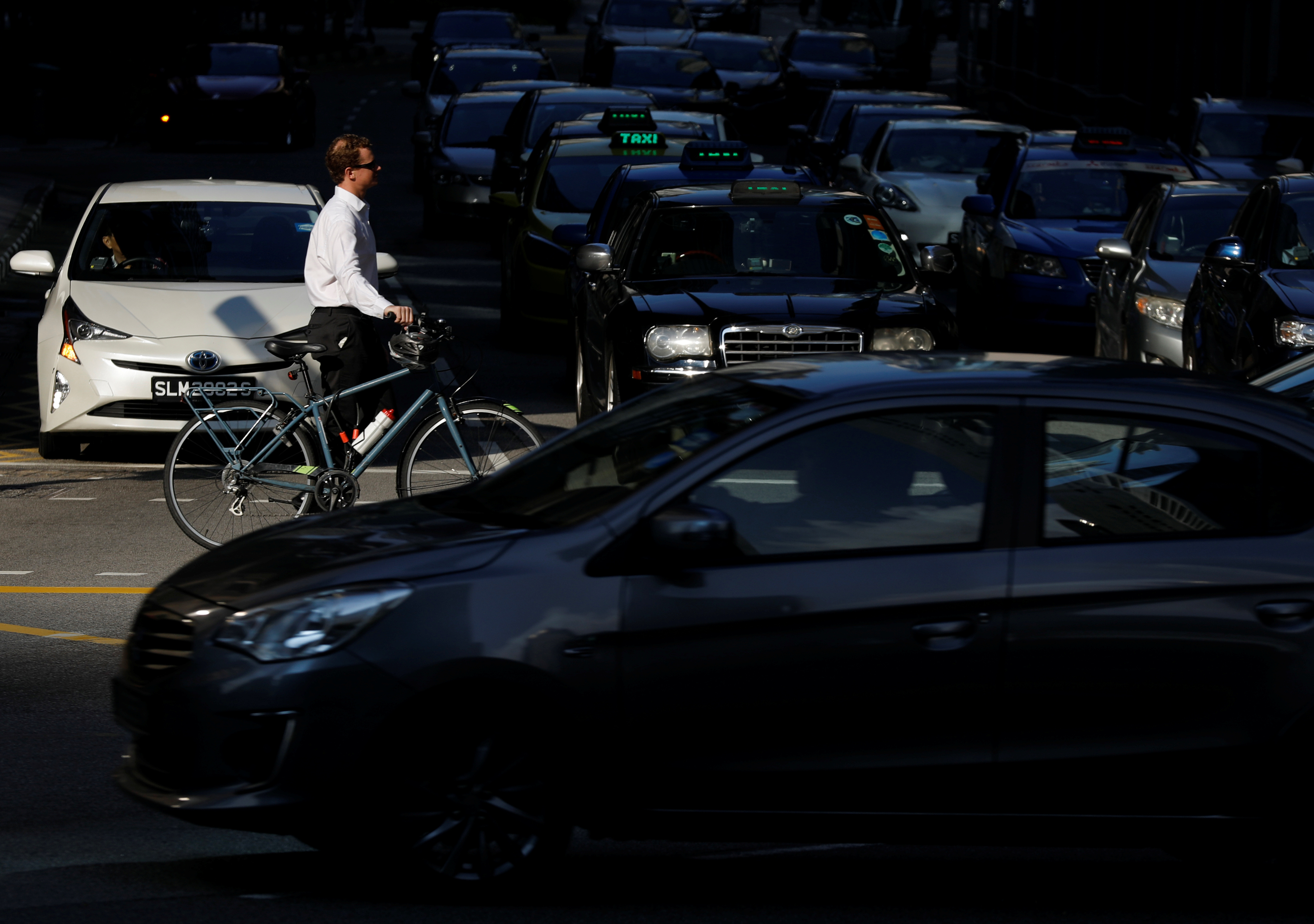 A commuter pushes his bicycle past cars stopping at a traffic light during morning rush hour in Singapore