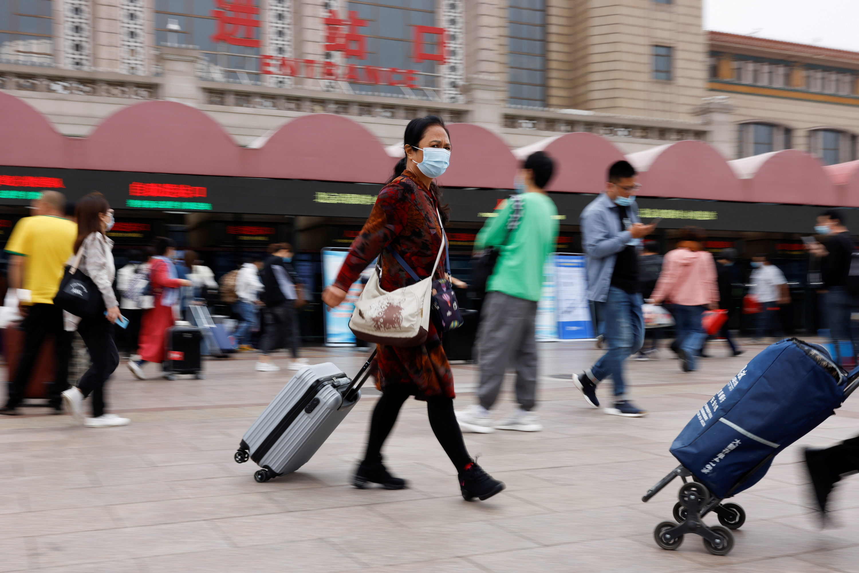 People walk with their luggage outside the Beijing Railway Station ahead of China's National Day and the upcoming Golden Week holiday, following the coronavirus disease (COVID-19) outbreak, in Beijing, China September 30, 2021. REUTERS/Carlos Garcia Rawlins