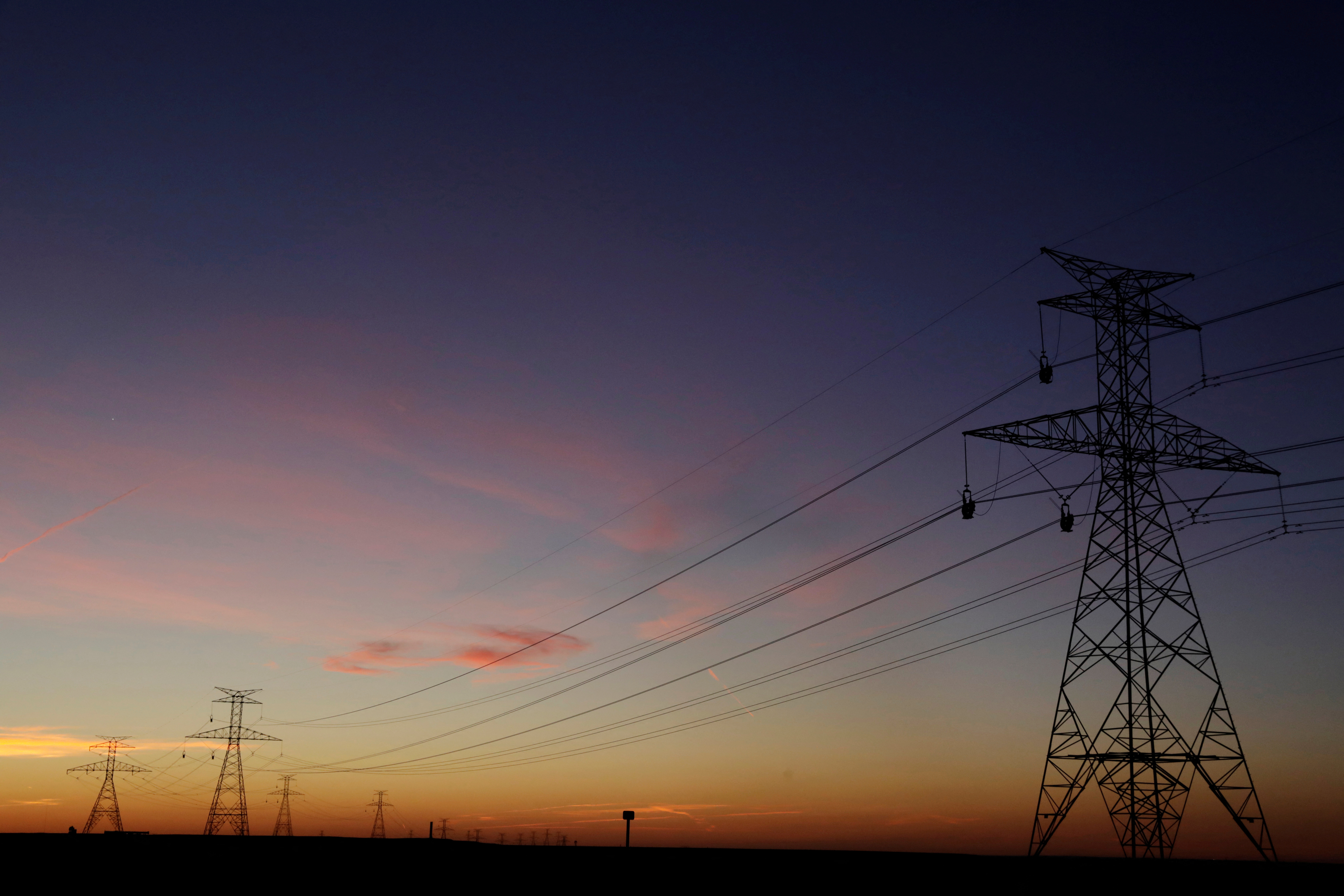 The sun sets behind power lines above the plains north of Amarillo, Texas