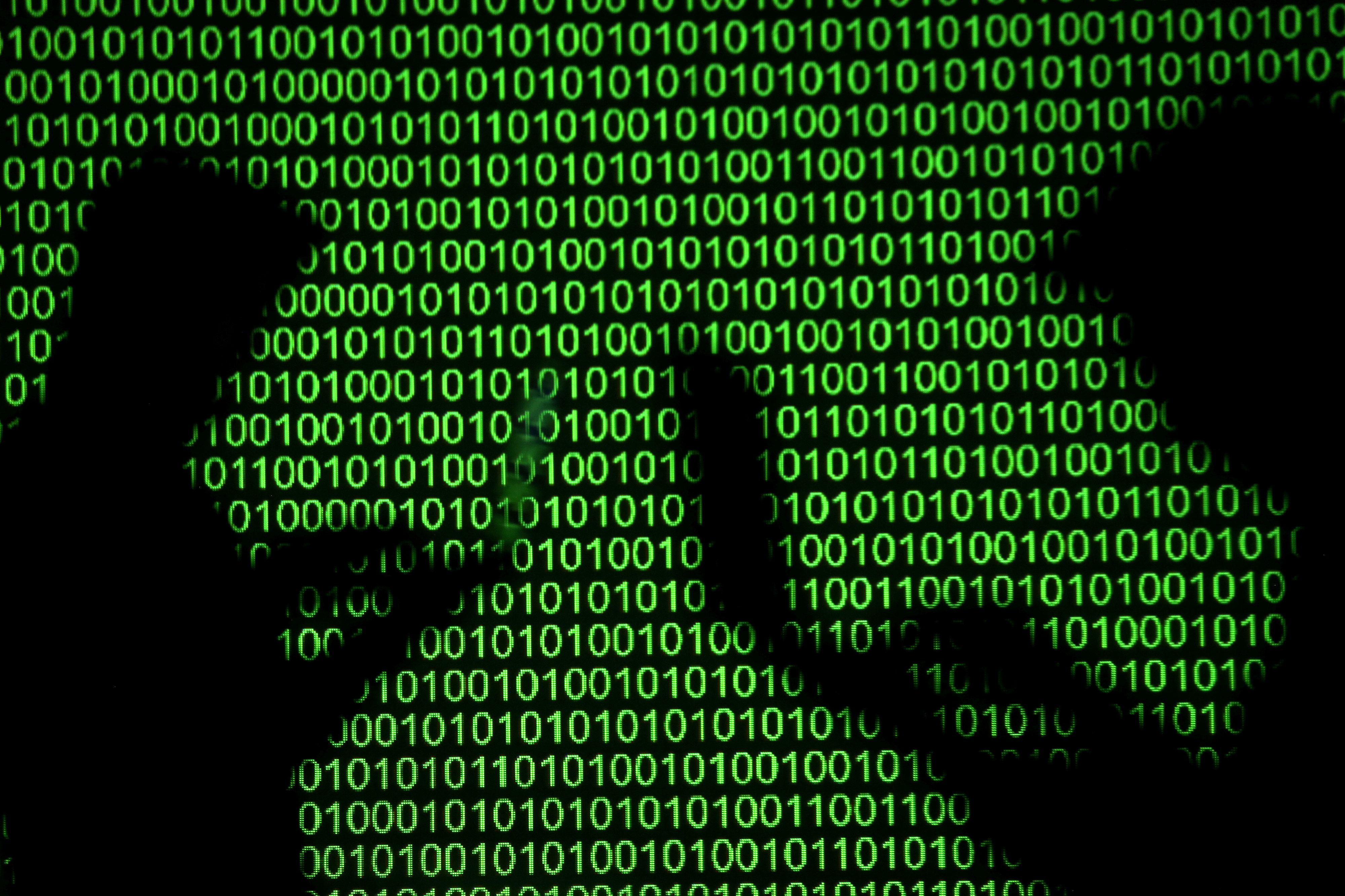 Silhouettes of laptop users are seen next to a screen projection of binary code are seen in this picture illustration