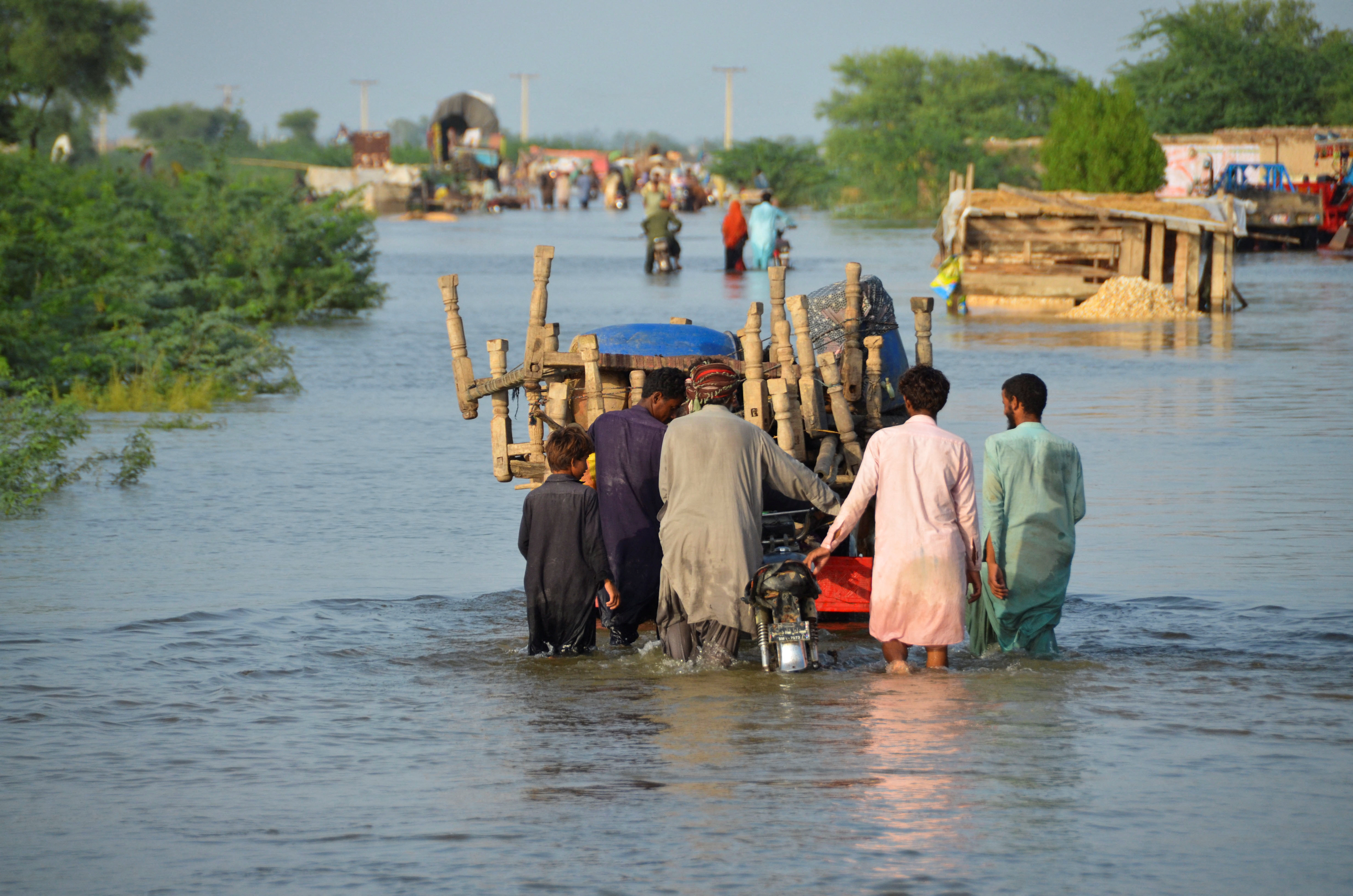 Men walk along a flooded road with their belongings, following rains and floods during the monsoon season in Sohbatpur