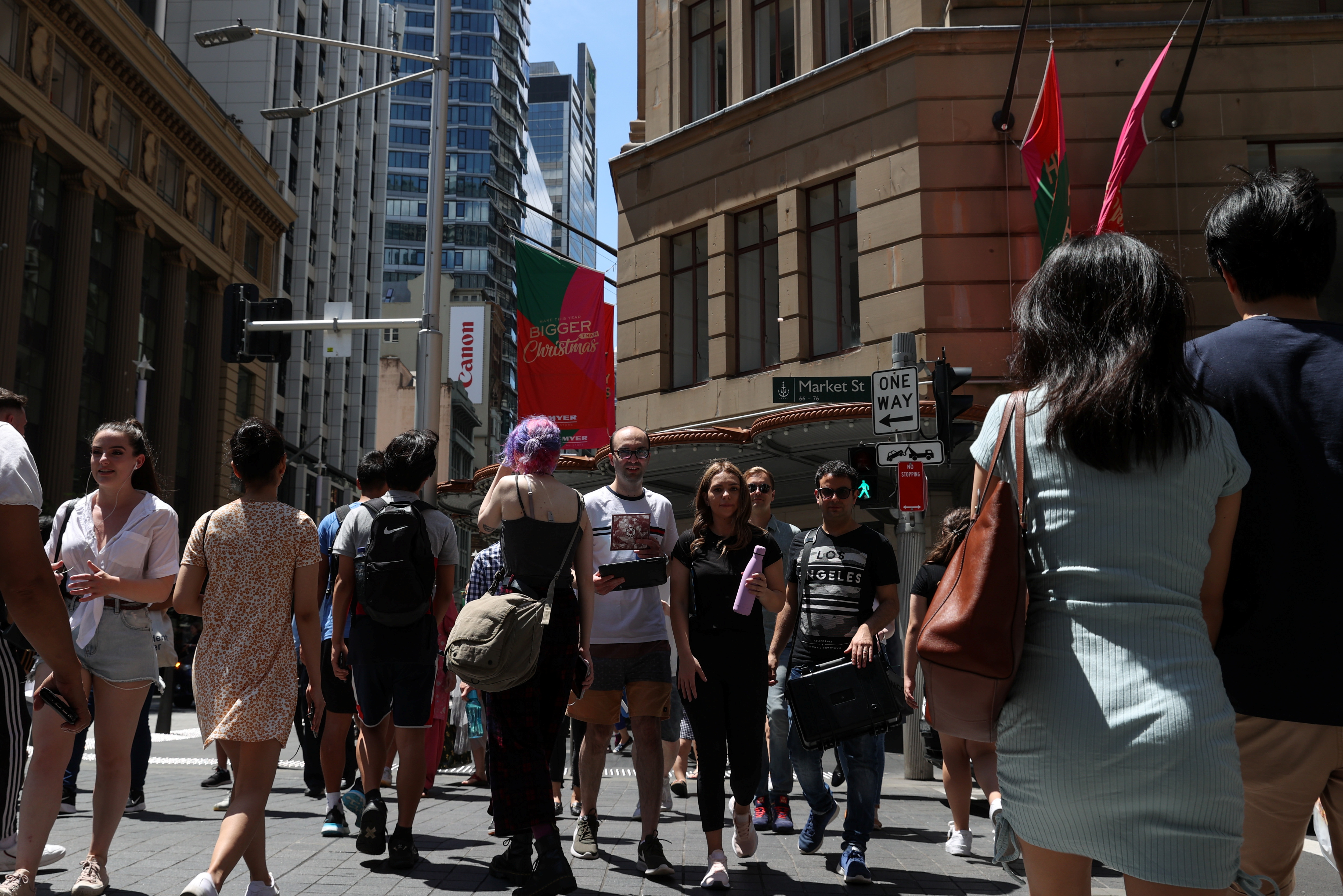 People cross a busy street under holiday decorations in the city centre of Sydney