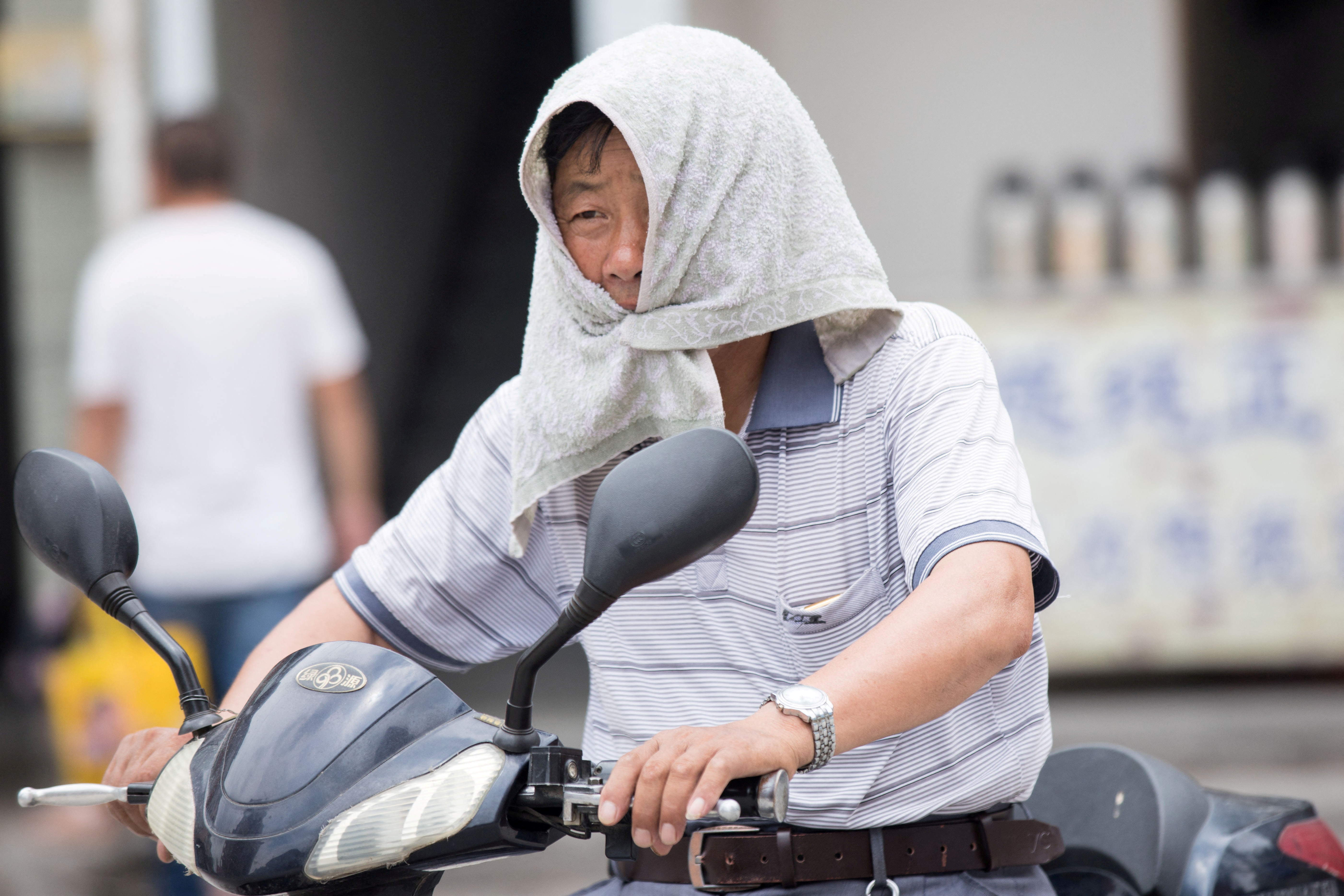 A man is seen with a towel tied around his head to escape hot weather as a heat wave hits Hangzhou