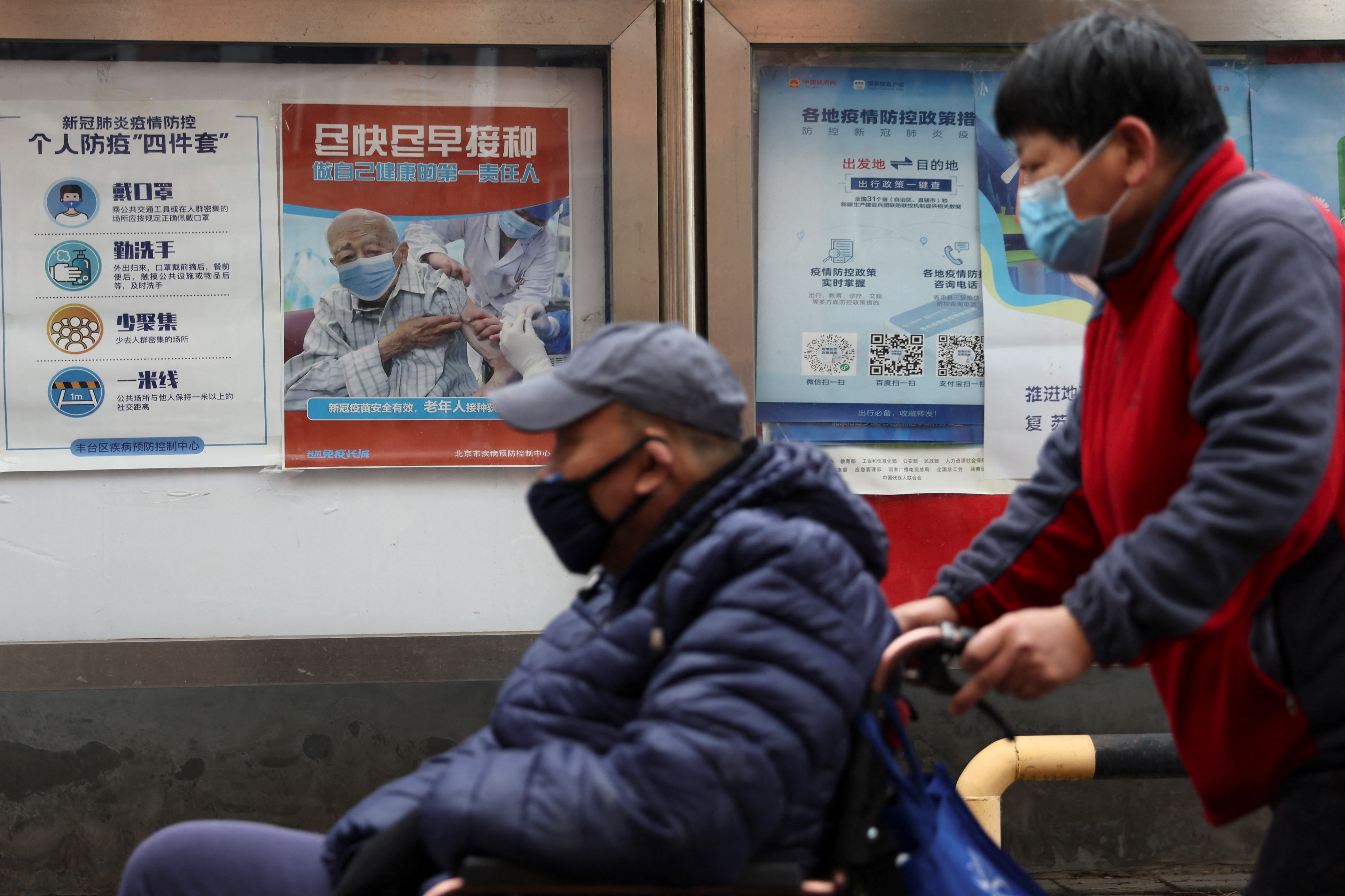 People pass by a poster encouraging elderly people to get vaccinated against COVID-19, in Beijing