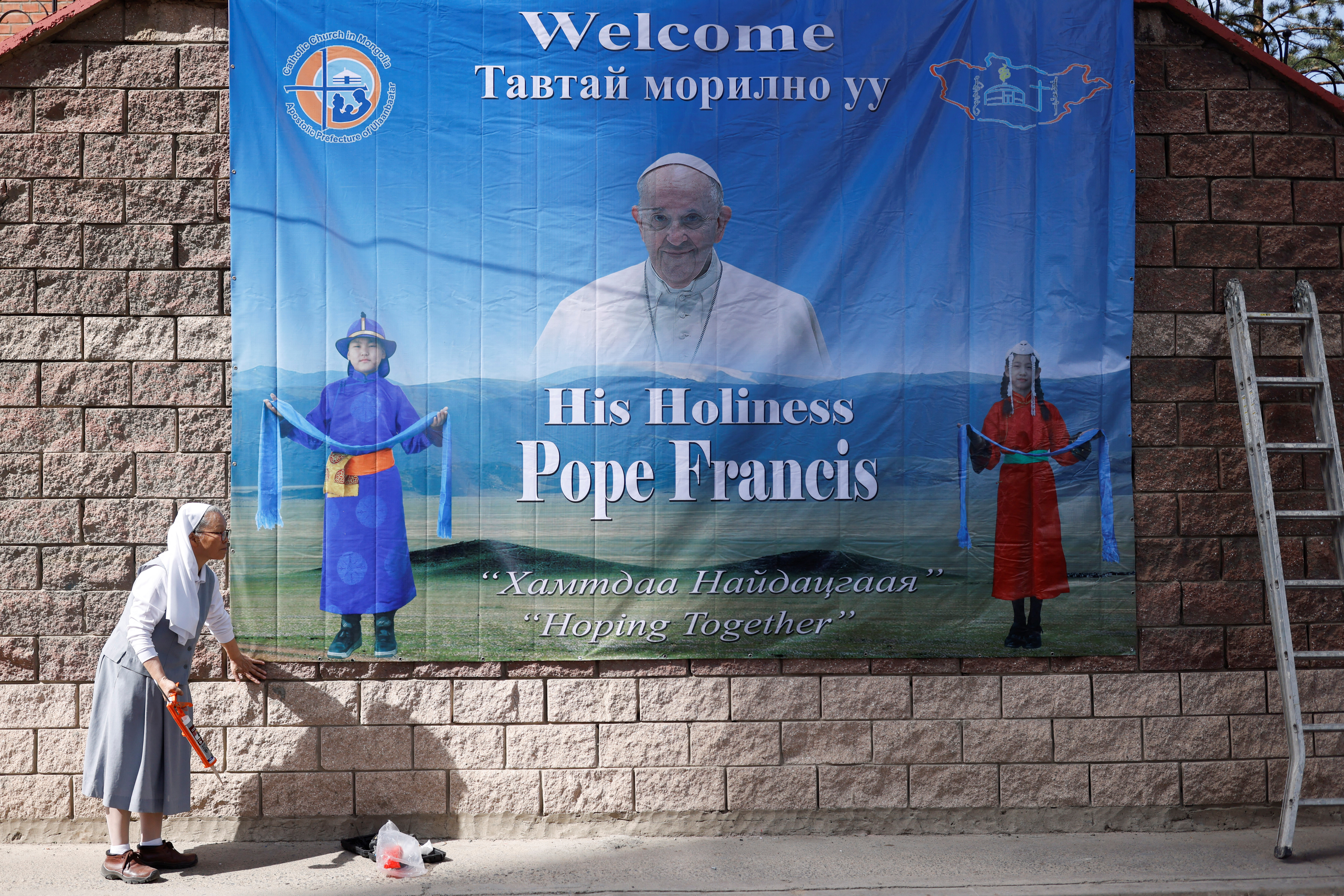 A nun installs a poster with an image of Pope Francis outside the bishop’s house, where he is expected to stay during his Apostolic Journey, one day ahead of his arrival in Ulaanbaatar