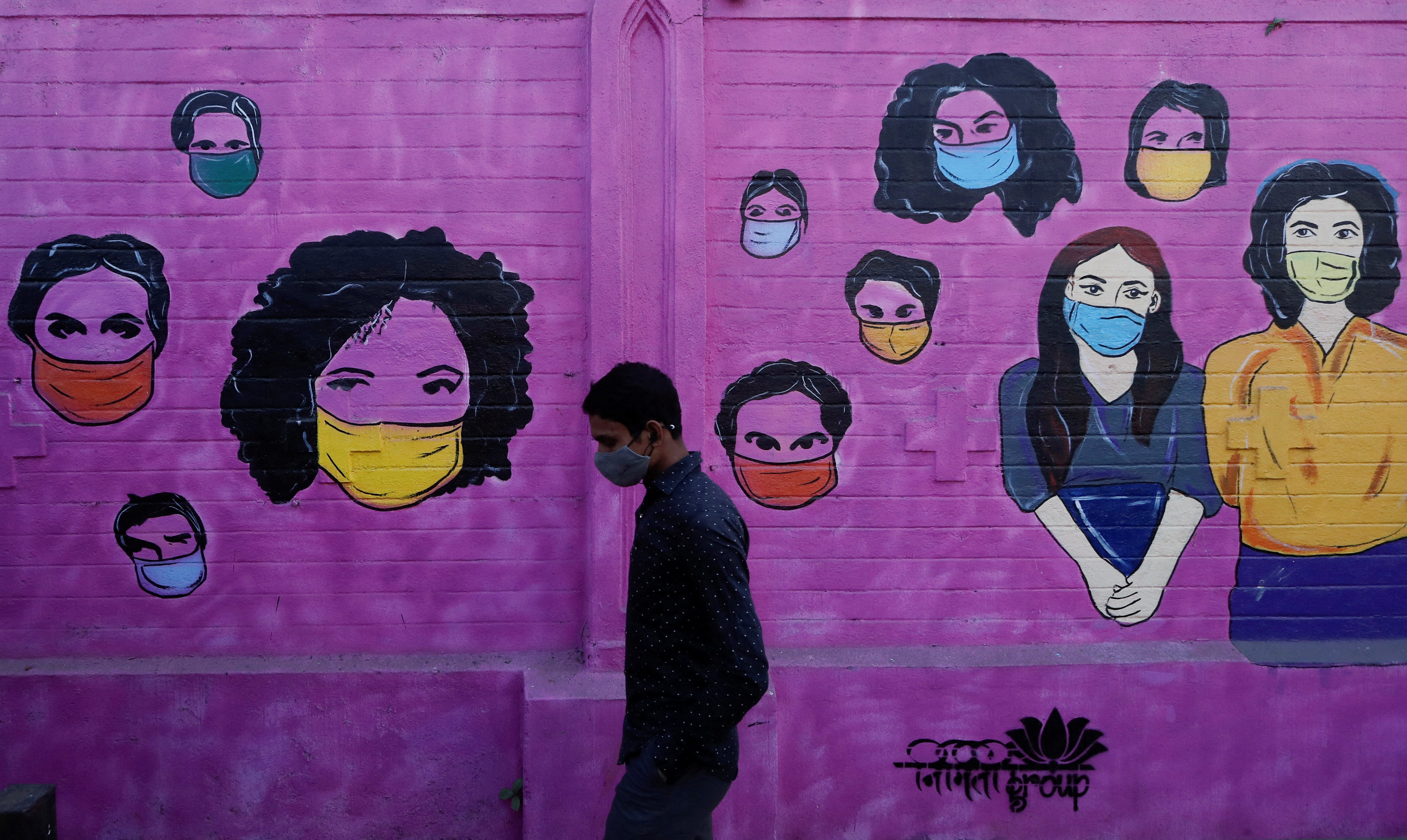 A man wearing a protective face mask walks past a mural on a street, amidst the spread of COVID-19, in Mumbai