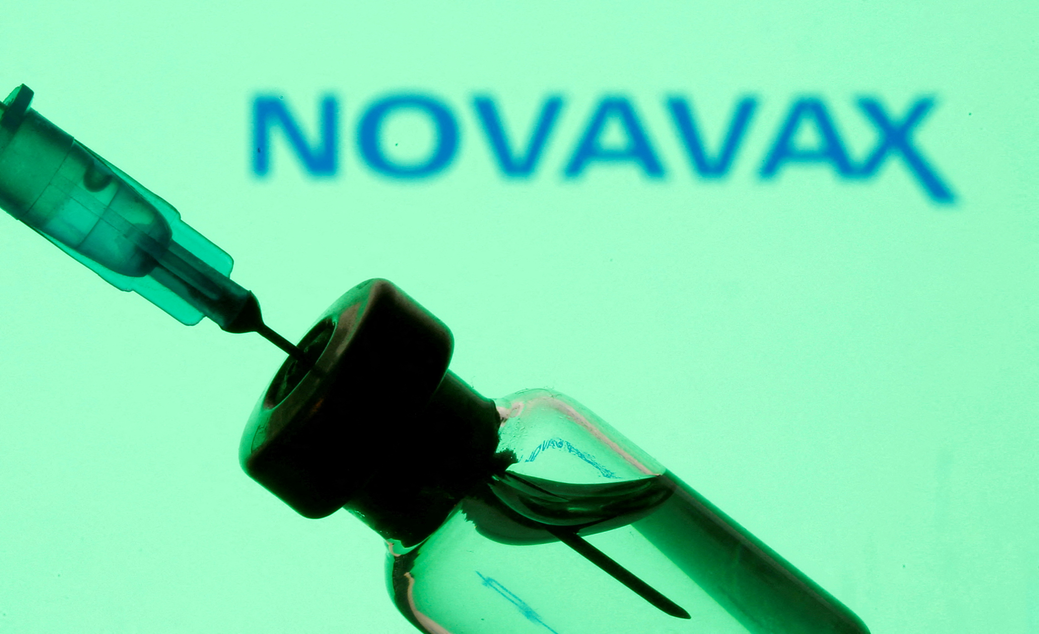 A vial and sryinge are seen in front of displayed Novavax logo in this illustration